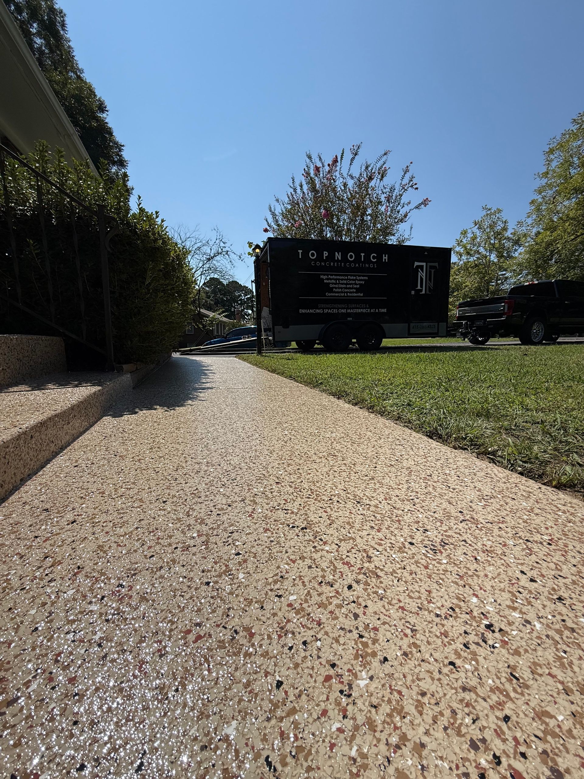 Gravel driveway beside hedges leading to a black sign under a clear blue sky.