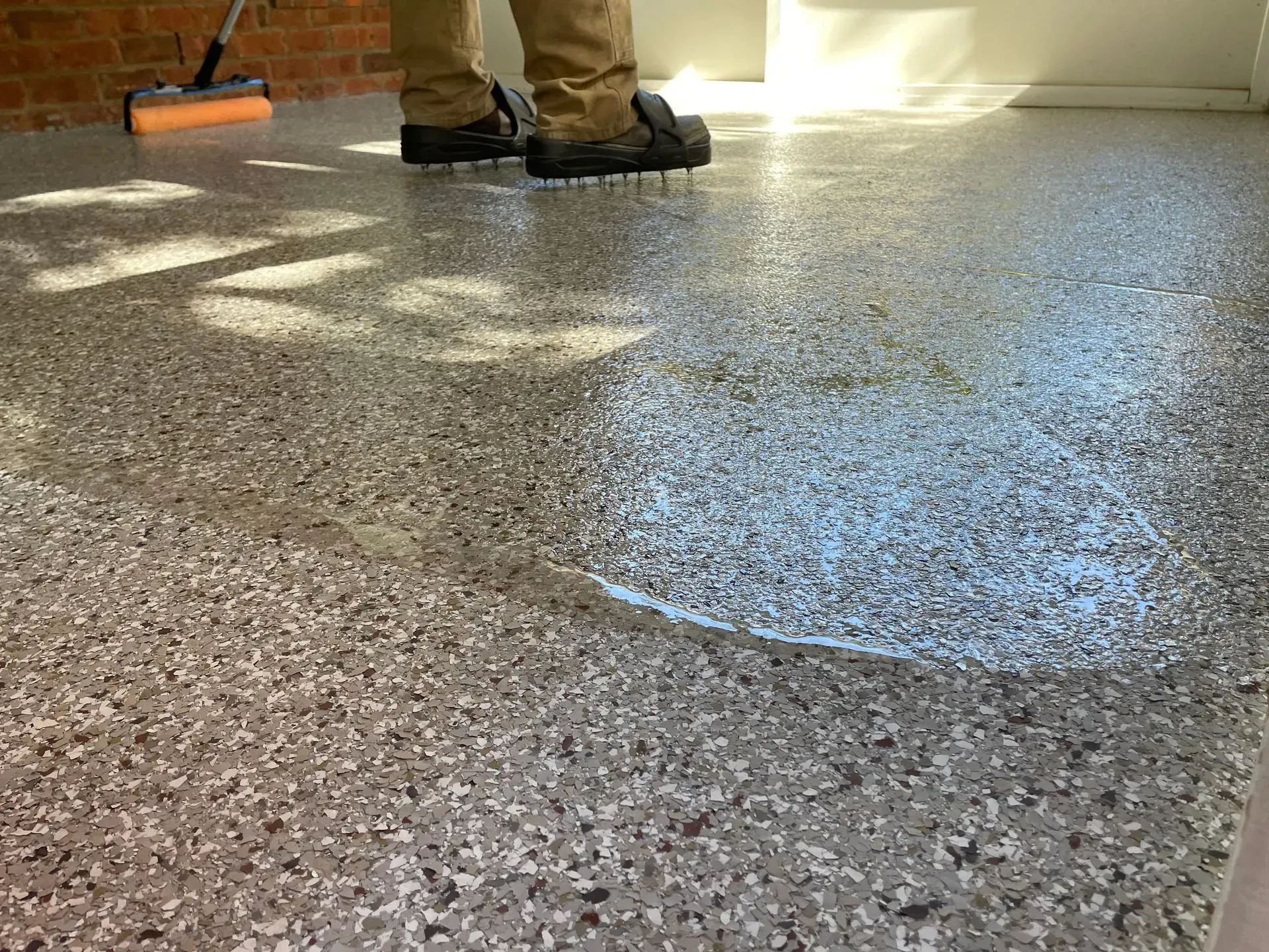 Person cleaning a speckled floor with a mop. The floor is wet and reflects sunlight.