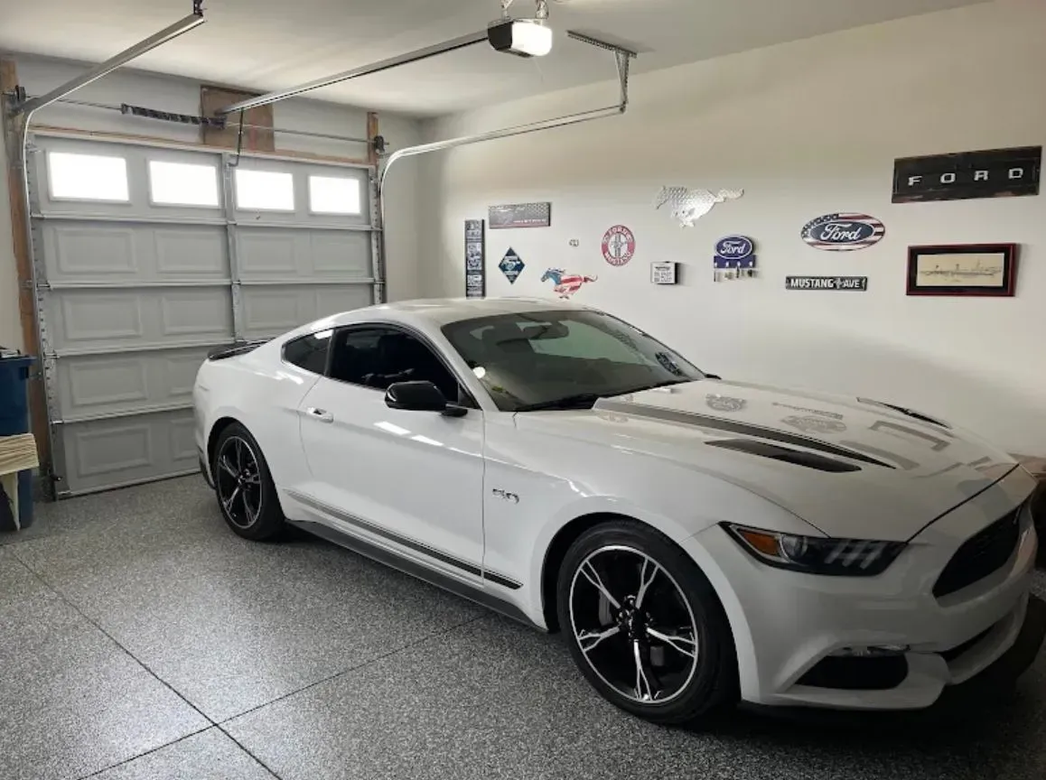 White Ford Mustang in a garage, with car-themed wall decor and a closed garage door.