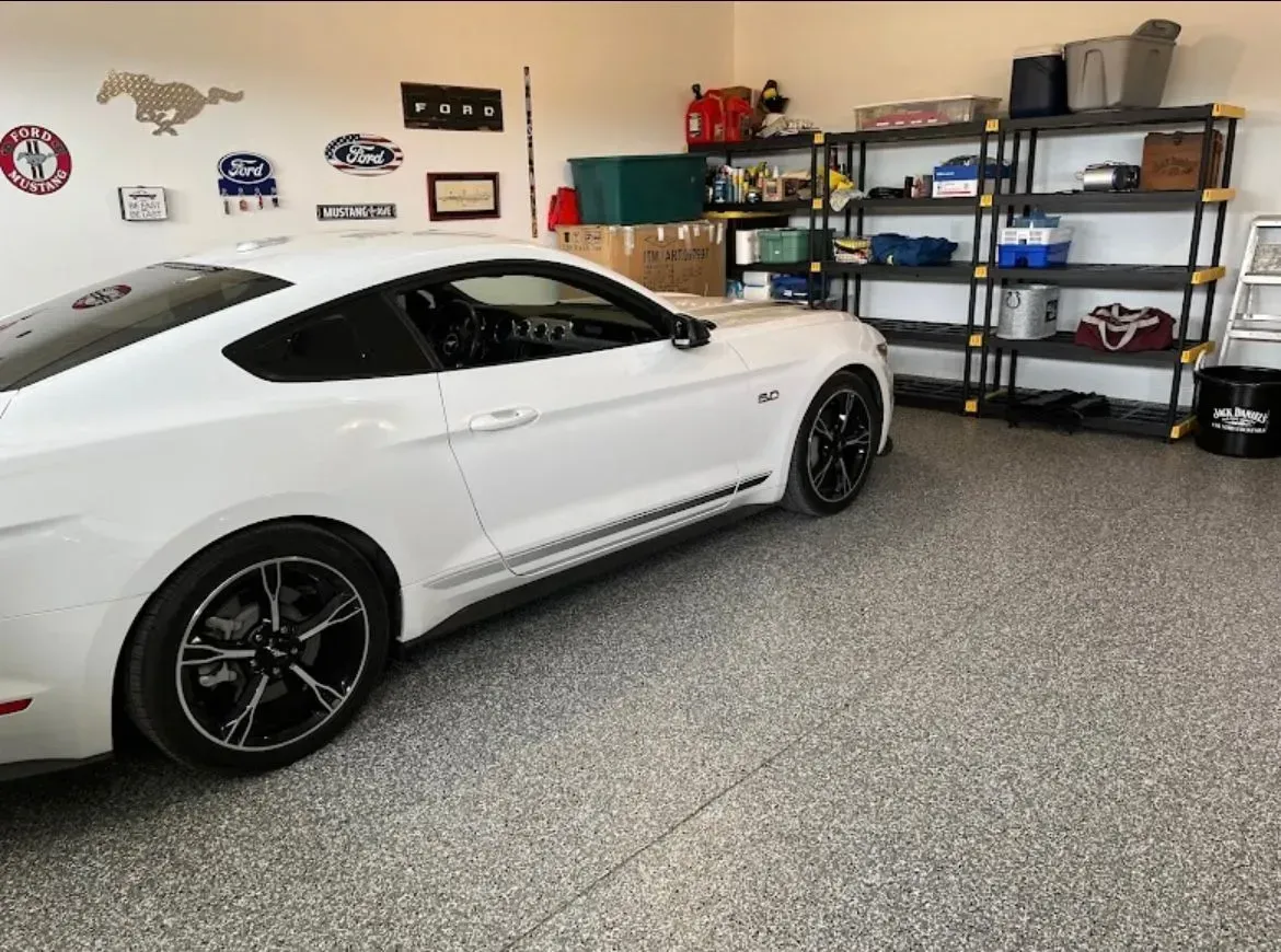 White Mustang parked in a garage with storage shelves, sporting goods, and decorative signs.