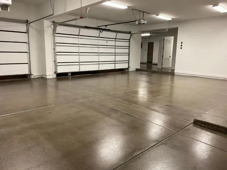 Polished concrete garage with closed white doors, bright ceiling lights, and a hallway.