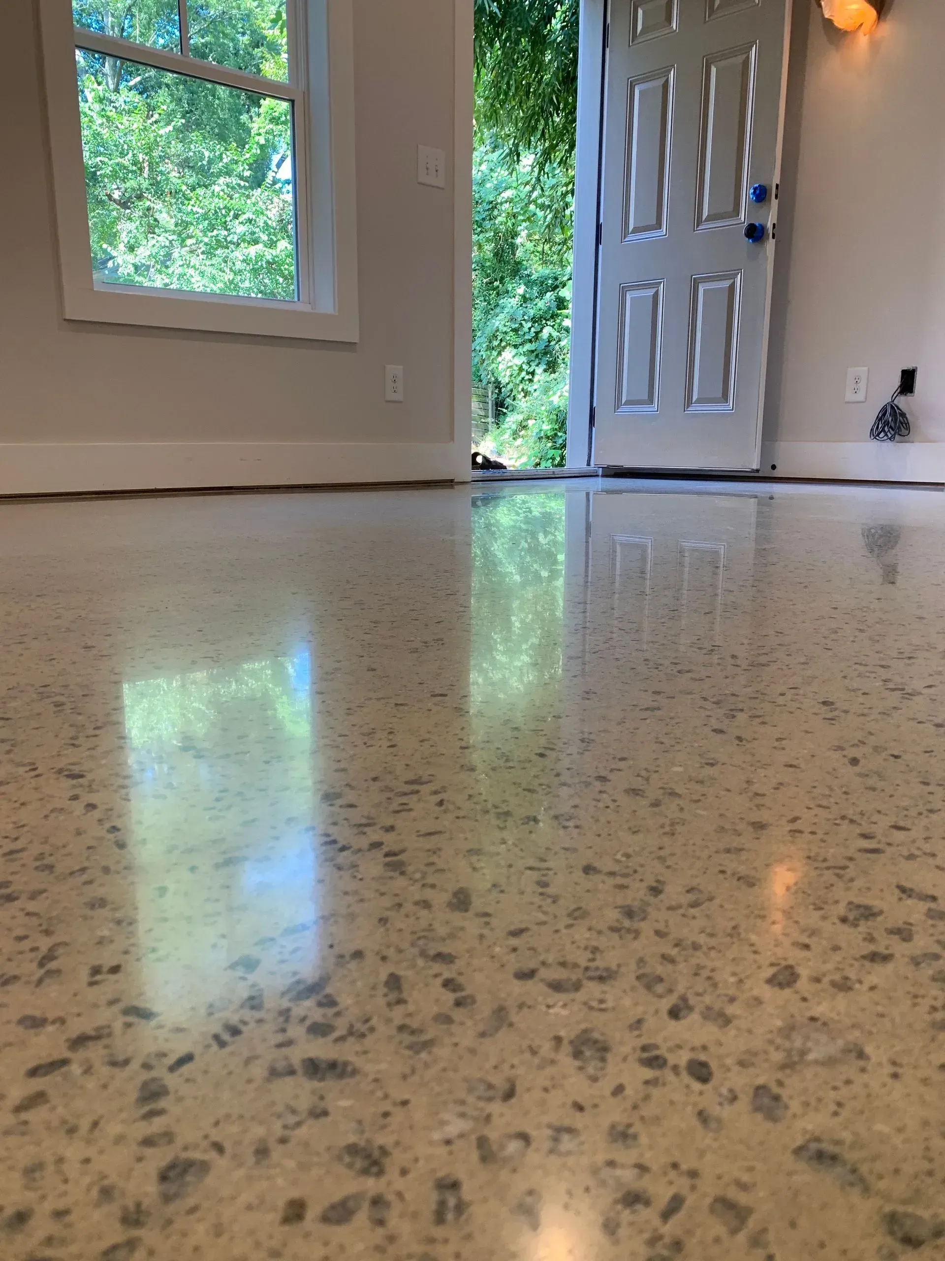 Polished concrete floor reflecting a door, window, and greenery; interior view.