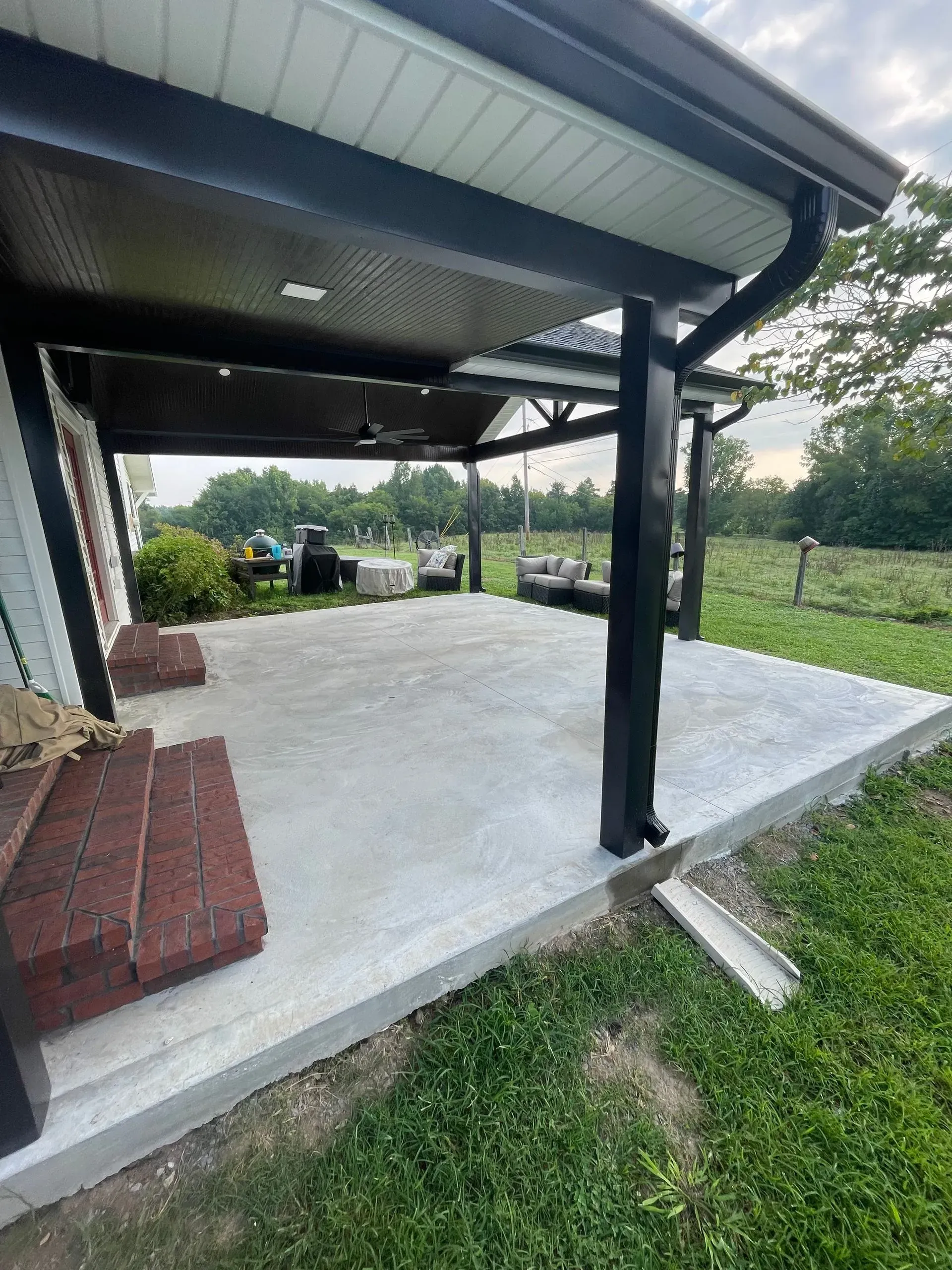 Covered concrete patio with black trim and brick steps.