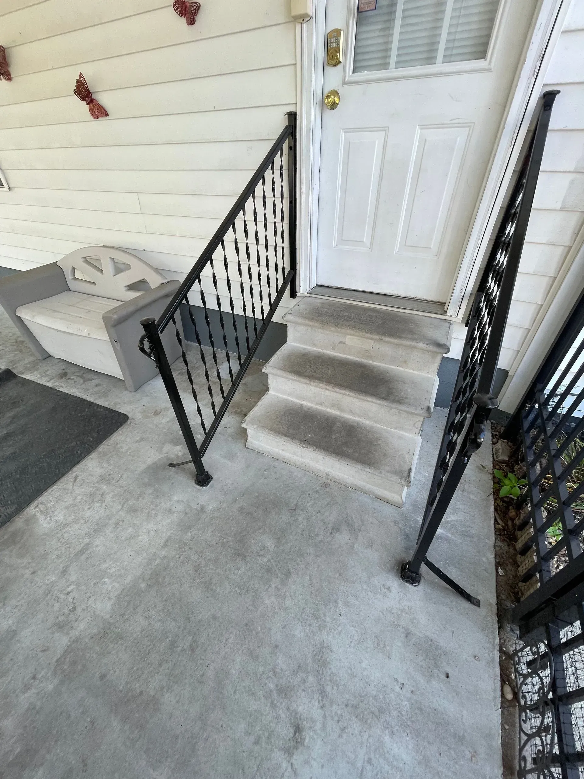 Exterior view of concrete steps leading to a white door, black metal railing on one side.