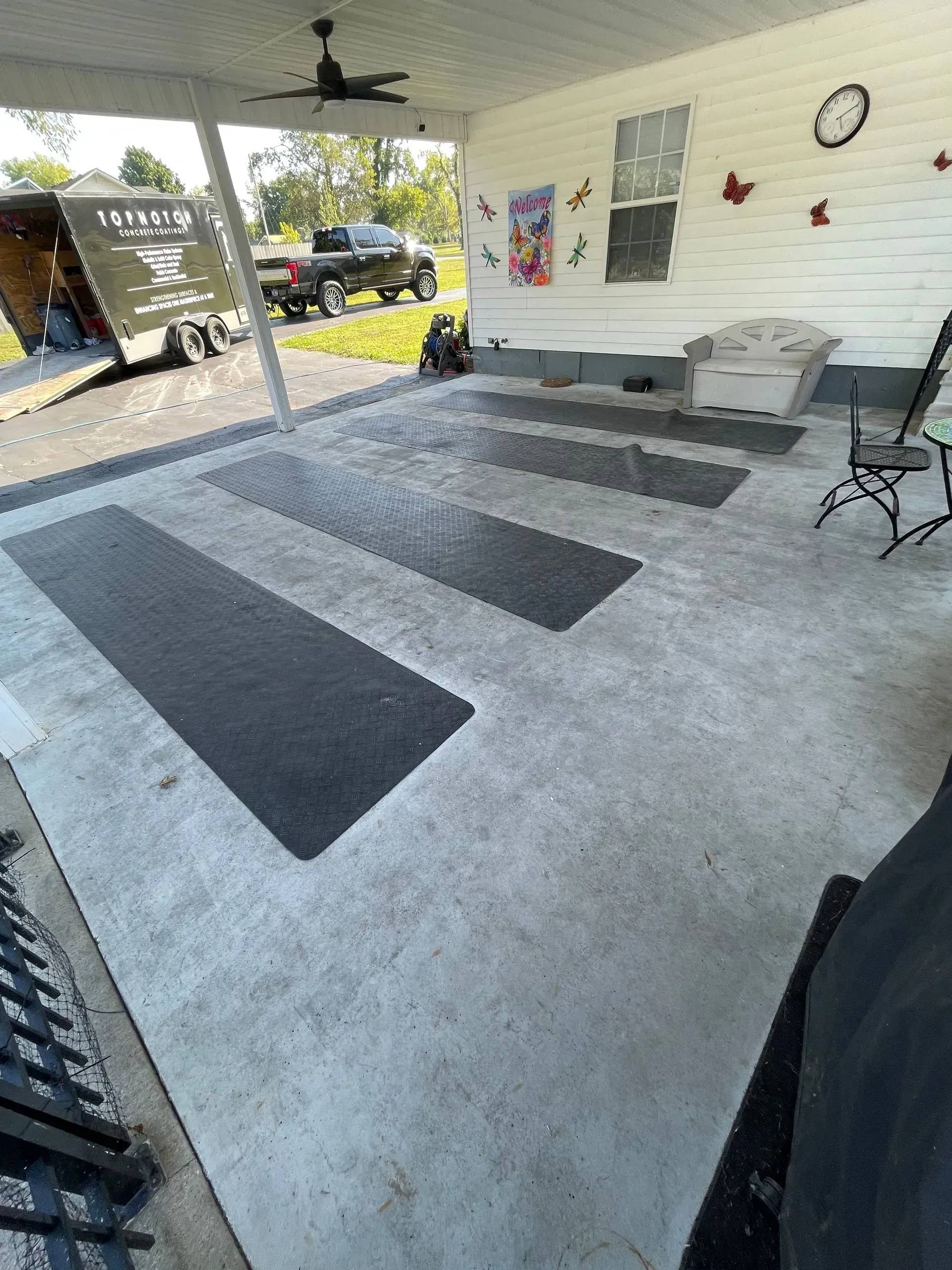 Concrete patio with dark rectangular rugs, a truck, and outdoor furniture.