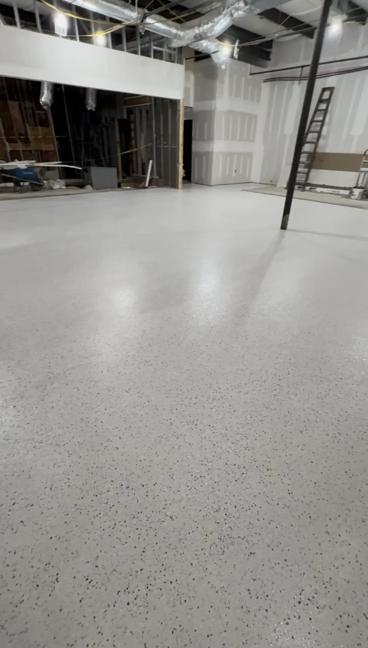 Empty, unfinished interior space with a light speckled concrete floor. Construction materials visible.