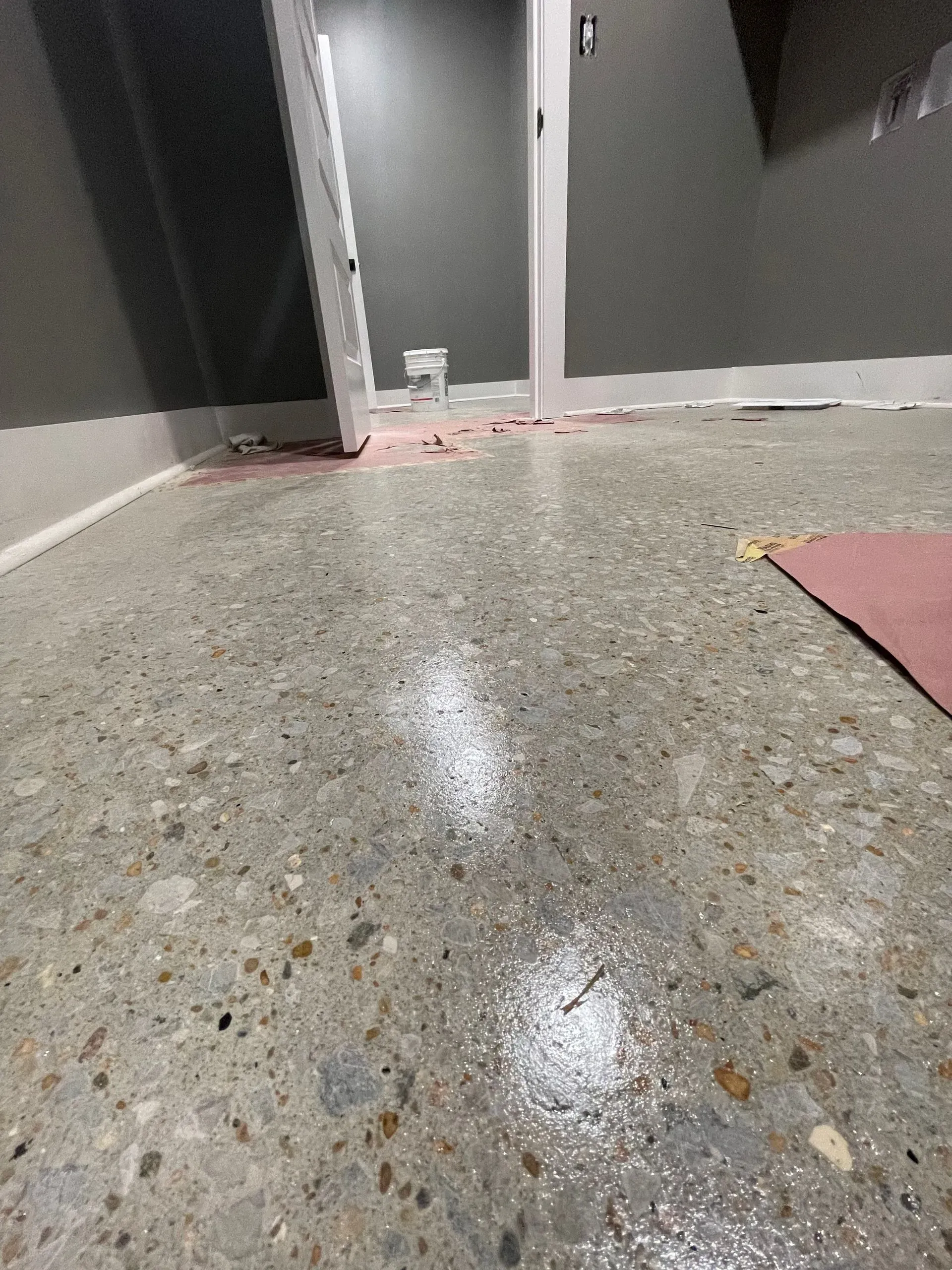 Concrete floor with wet patches, spills near a doorway and baseboard. Pink debris on the floor.