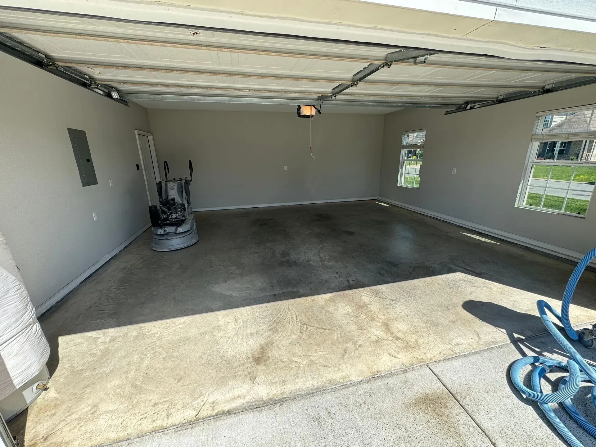 Interior of a garage with concrete floor and walls, a floor grinder, and two windows.