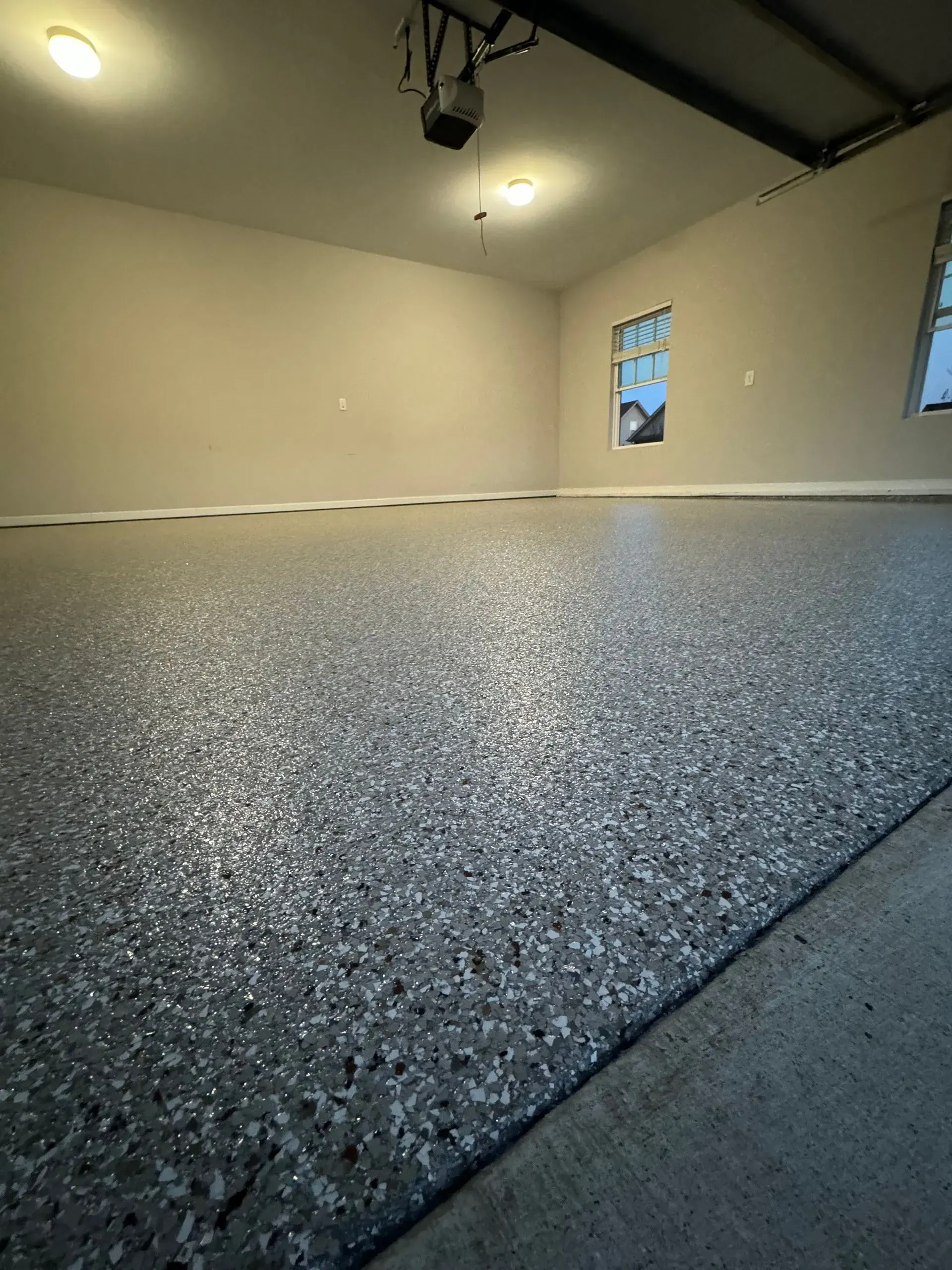 Empty garage with a gray epoxy floor. Interior shot with two windows and three ceiling lights.
