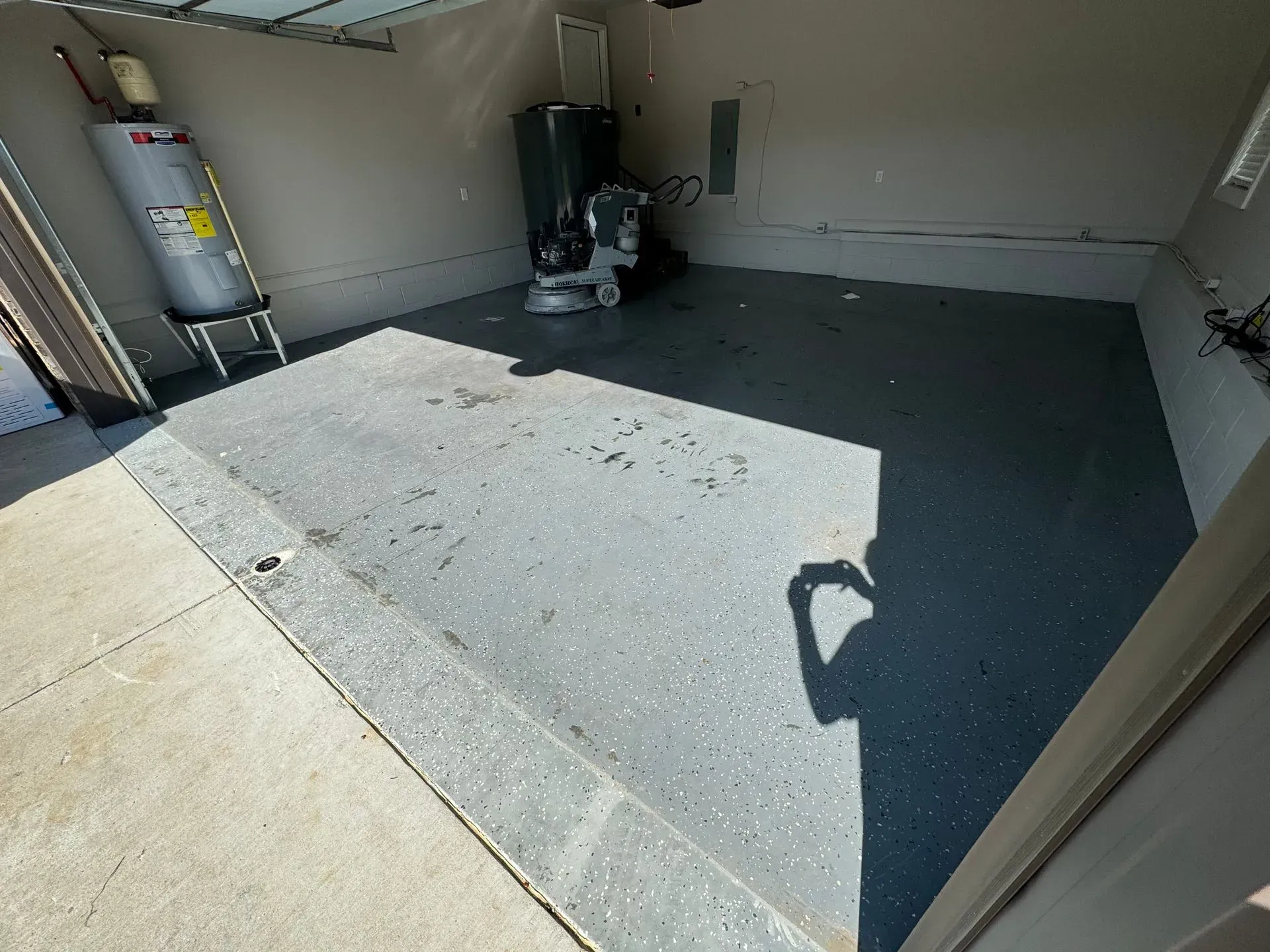 Garage interior with gray epoxy floor, water heater, and garage door opener. Shadows and bright sunlight.
