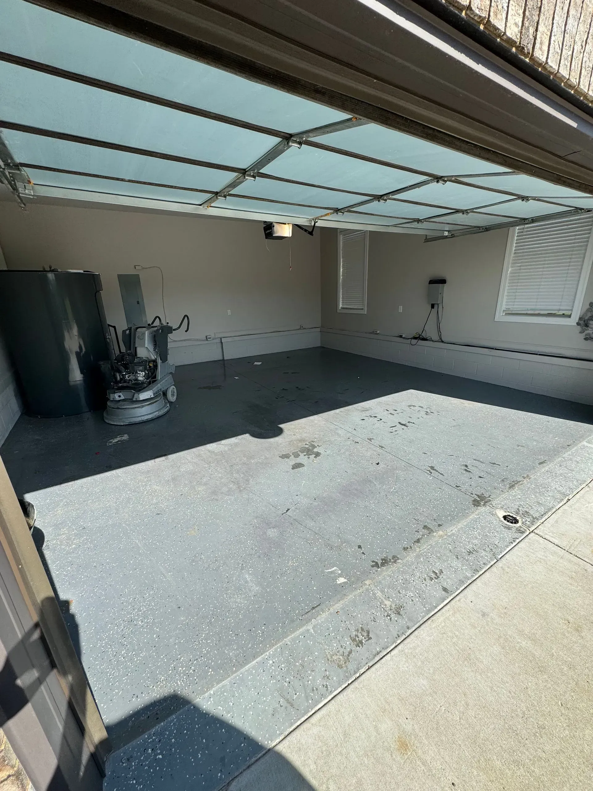 Empty gray garage with gray speckled floor; garage door open to exterior.