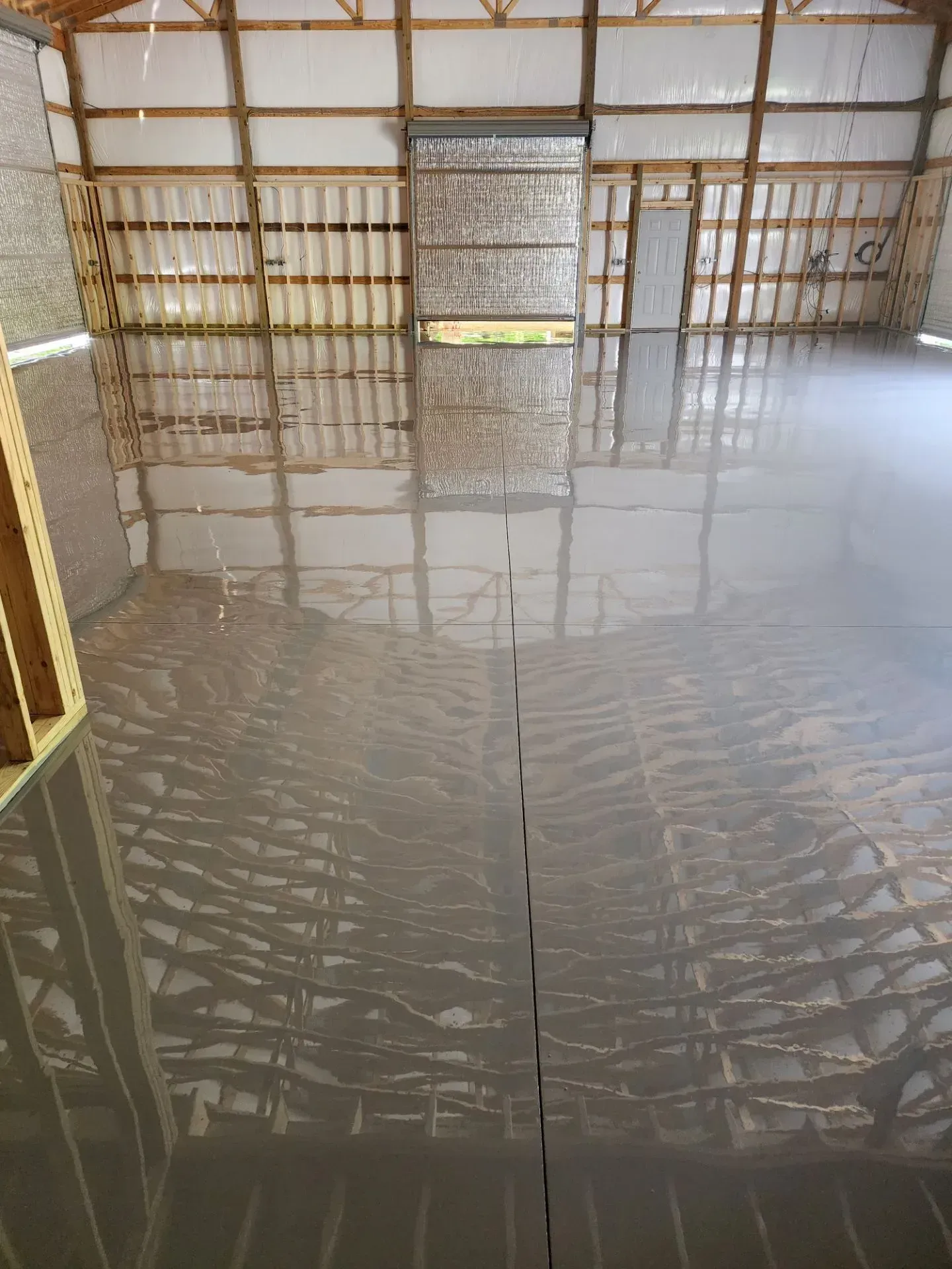 Interior of a barn with a shiny, wet concrete floor, reflecting the wooden beams and open doorway.