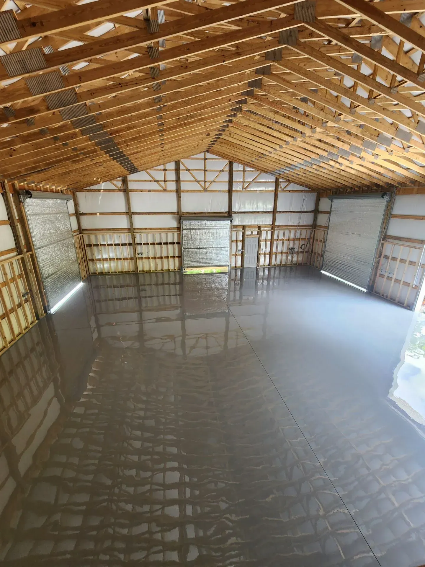 Interior of a large, empty building with a newly poured concrete floor, wooden beams, and natural light.
