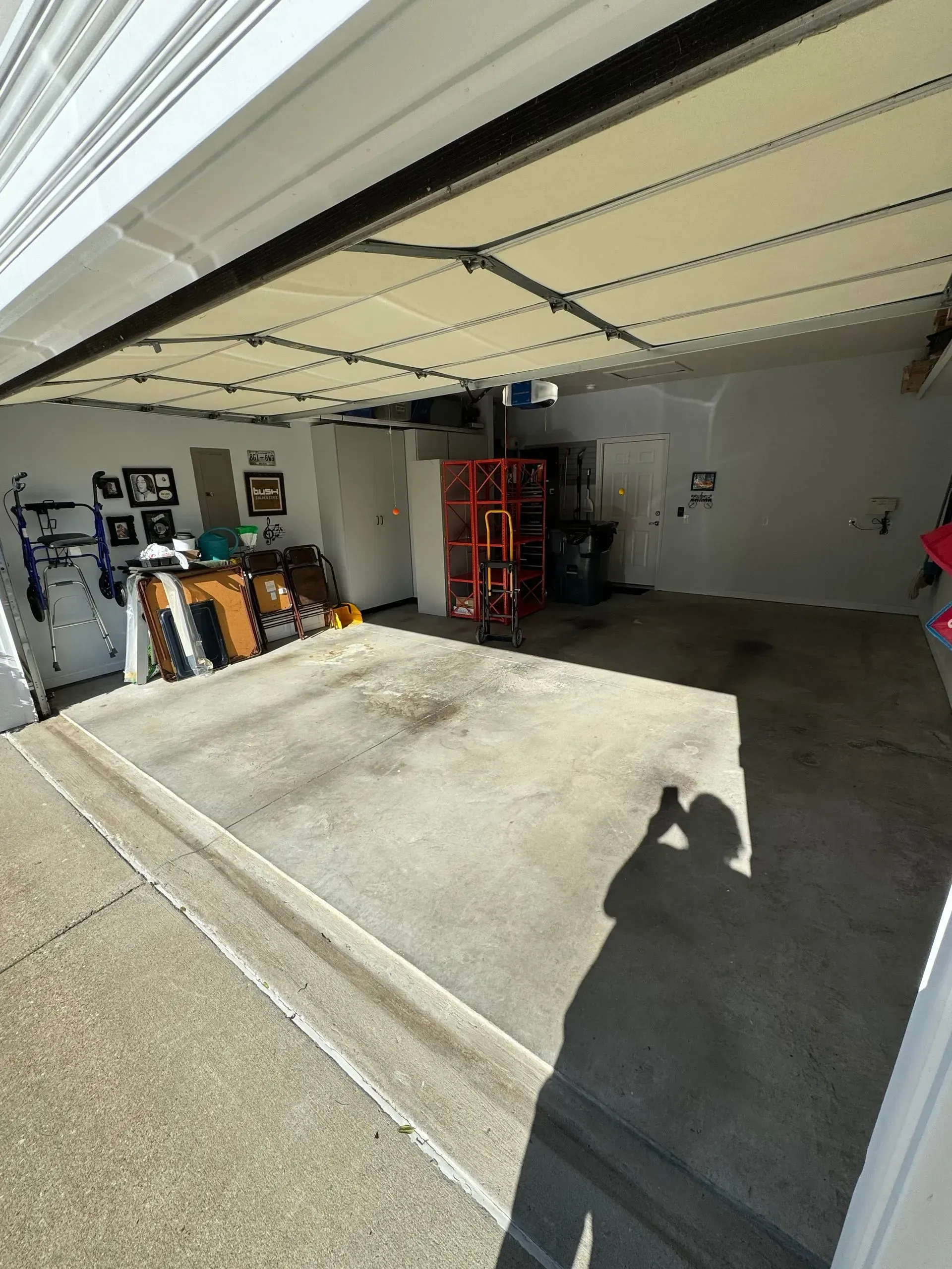 Open garage with concrete floor and shadow of person taking photo. Shelves, boxes, and a red object are visible inside.