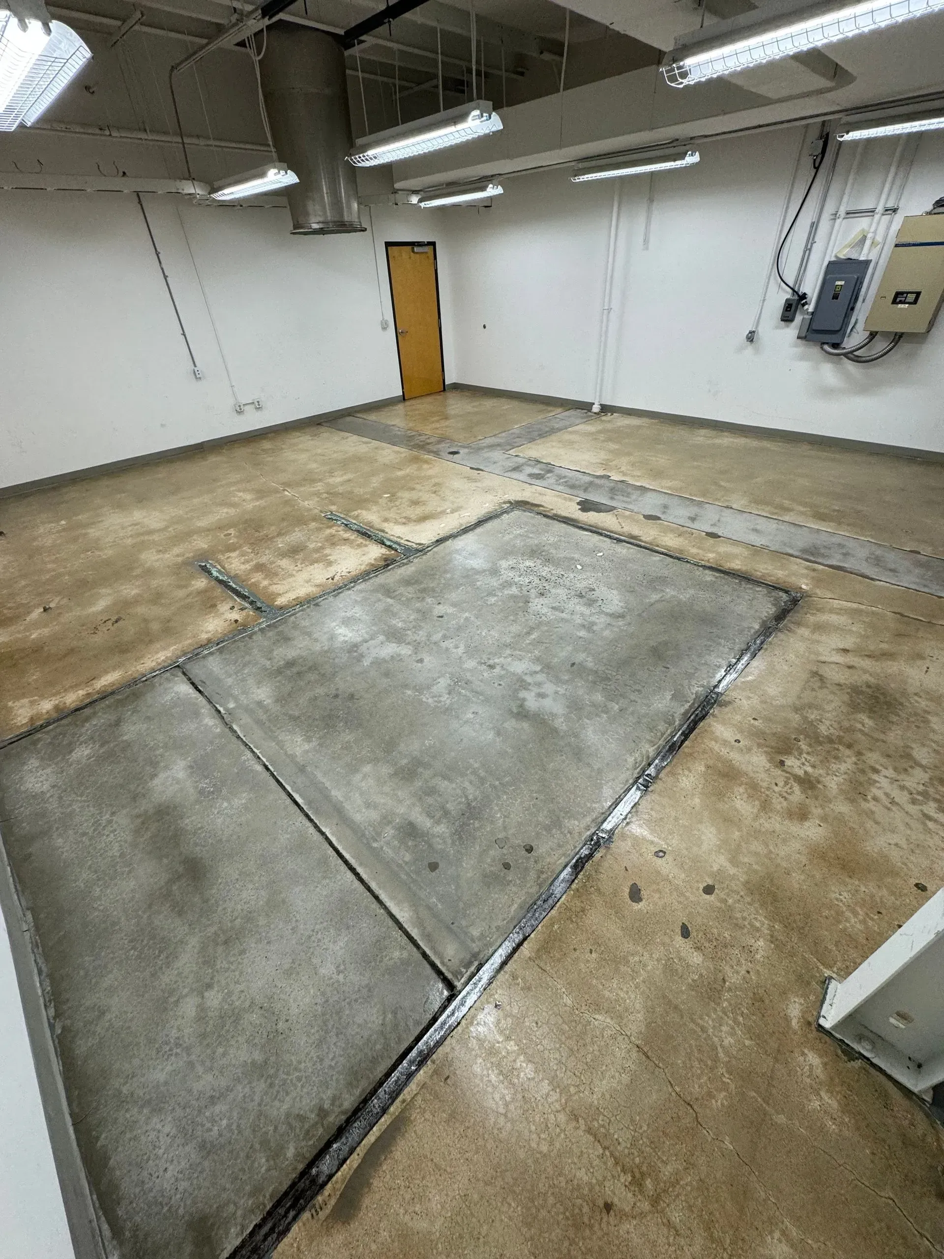 Empty room with concrete floor and insets, brown door, and electrical panel.
