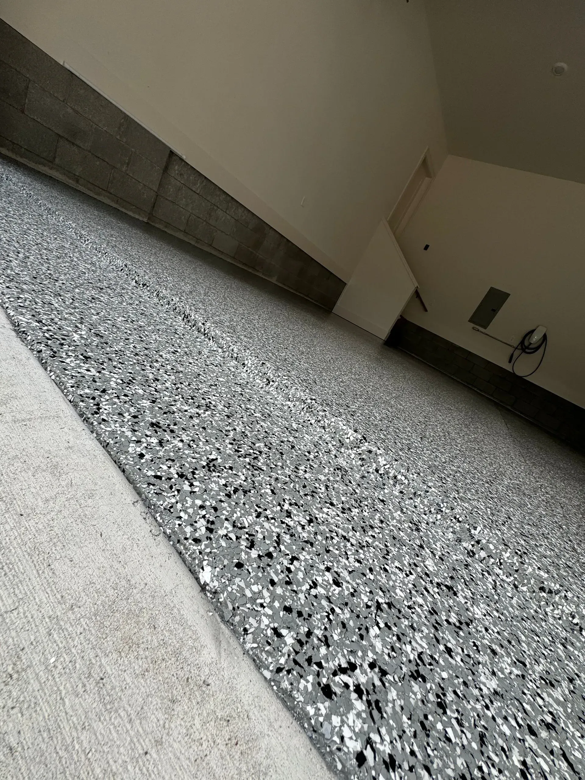 Garage floor with a speckled gray and white epoxy finish, a concrete border, and white walls.