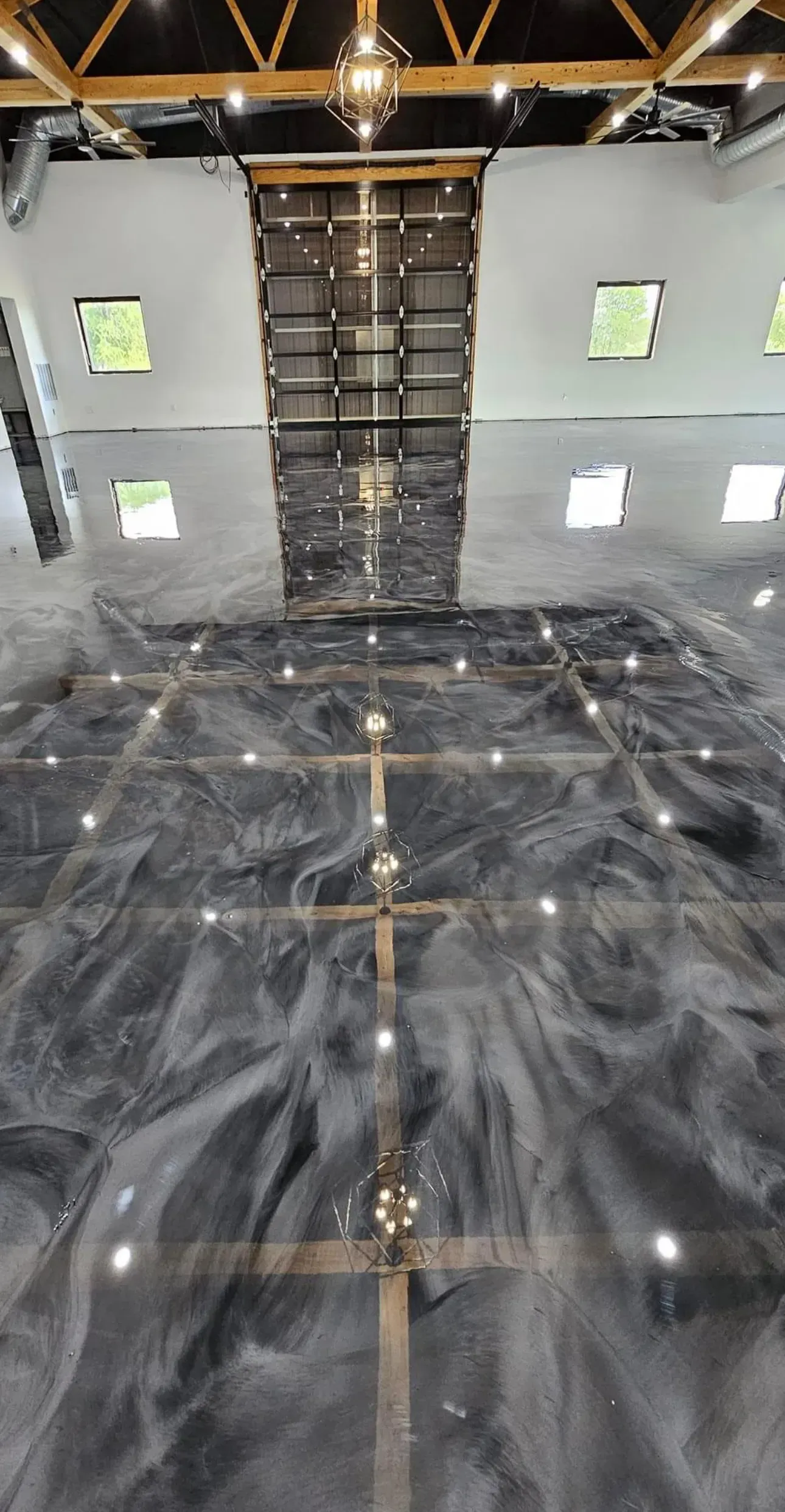 Epoxy floor with embedded lights, reflected in high-ceilinged room with rafters and white walls.