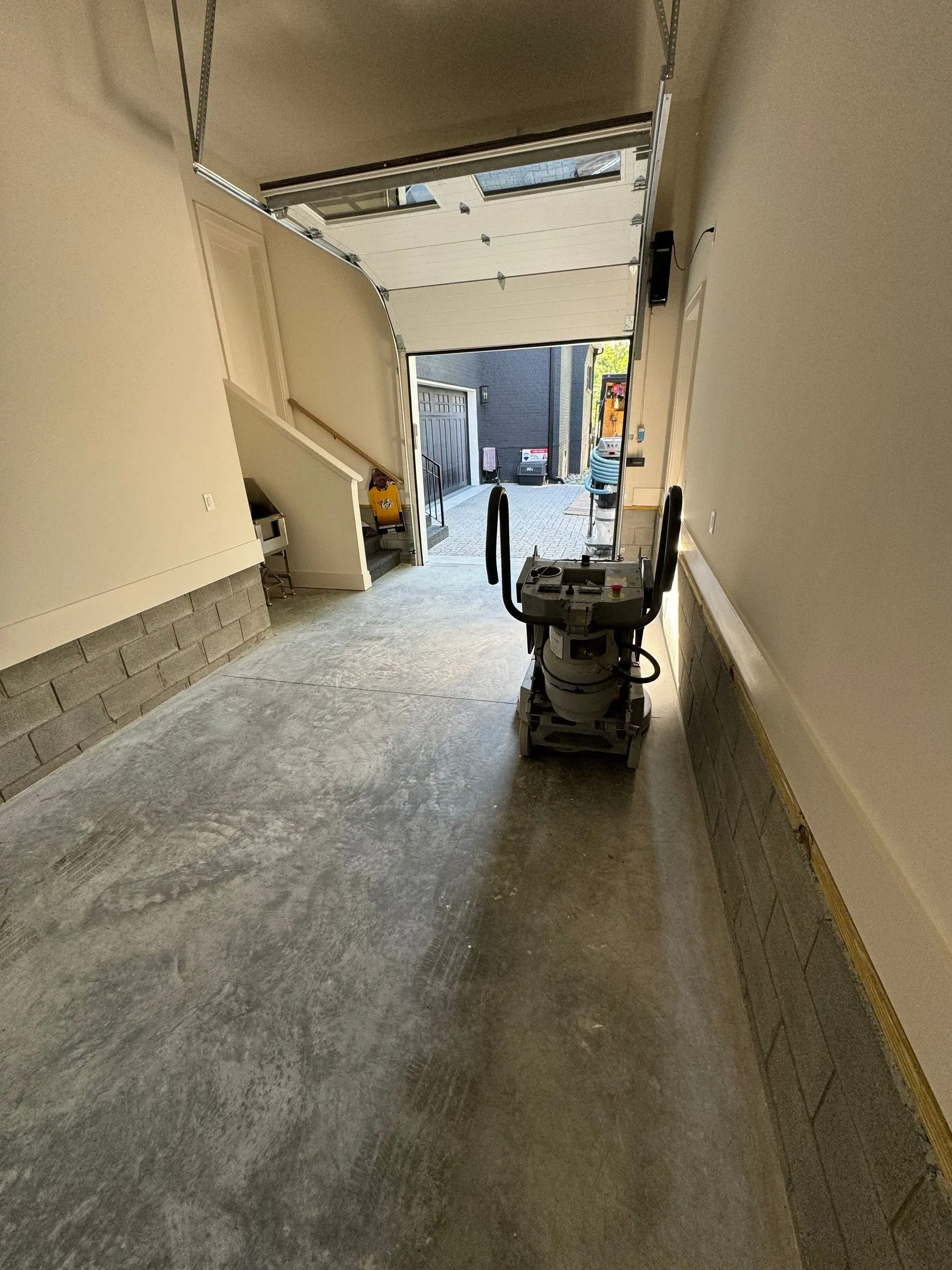 Construction site hallway with floor grinder; walls, concrete, light at end.