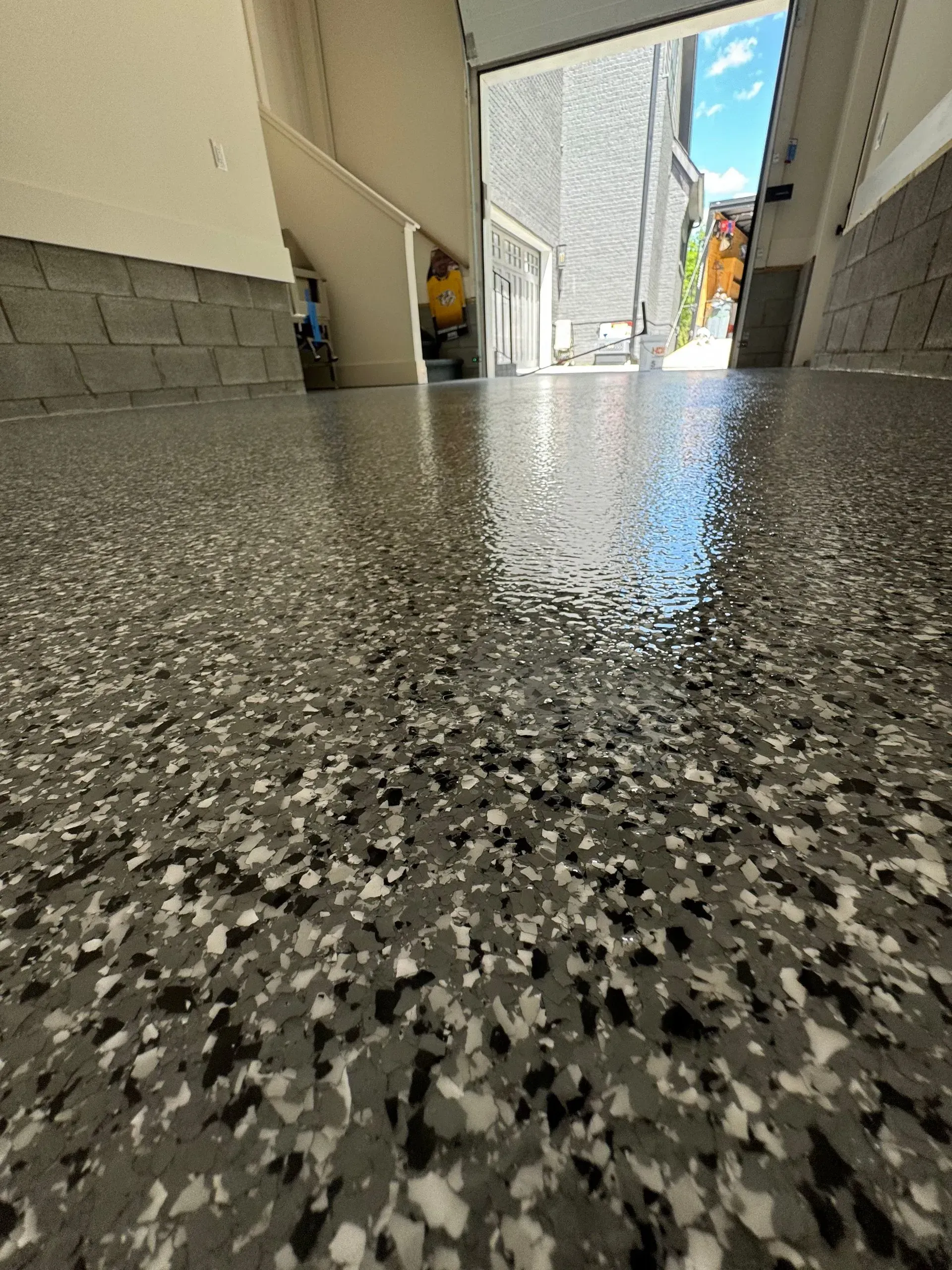 Close-up view of a newly coated garage floor with gray, black, and white flecks, with the open garage door in the background.
