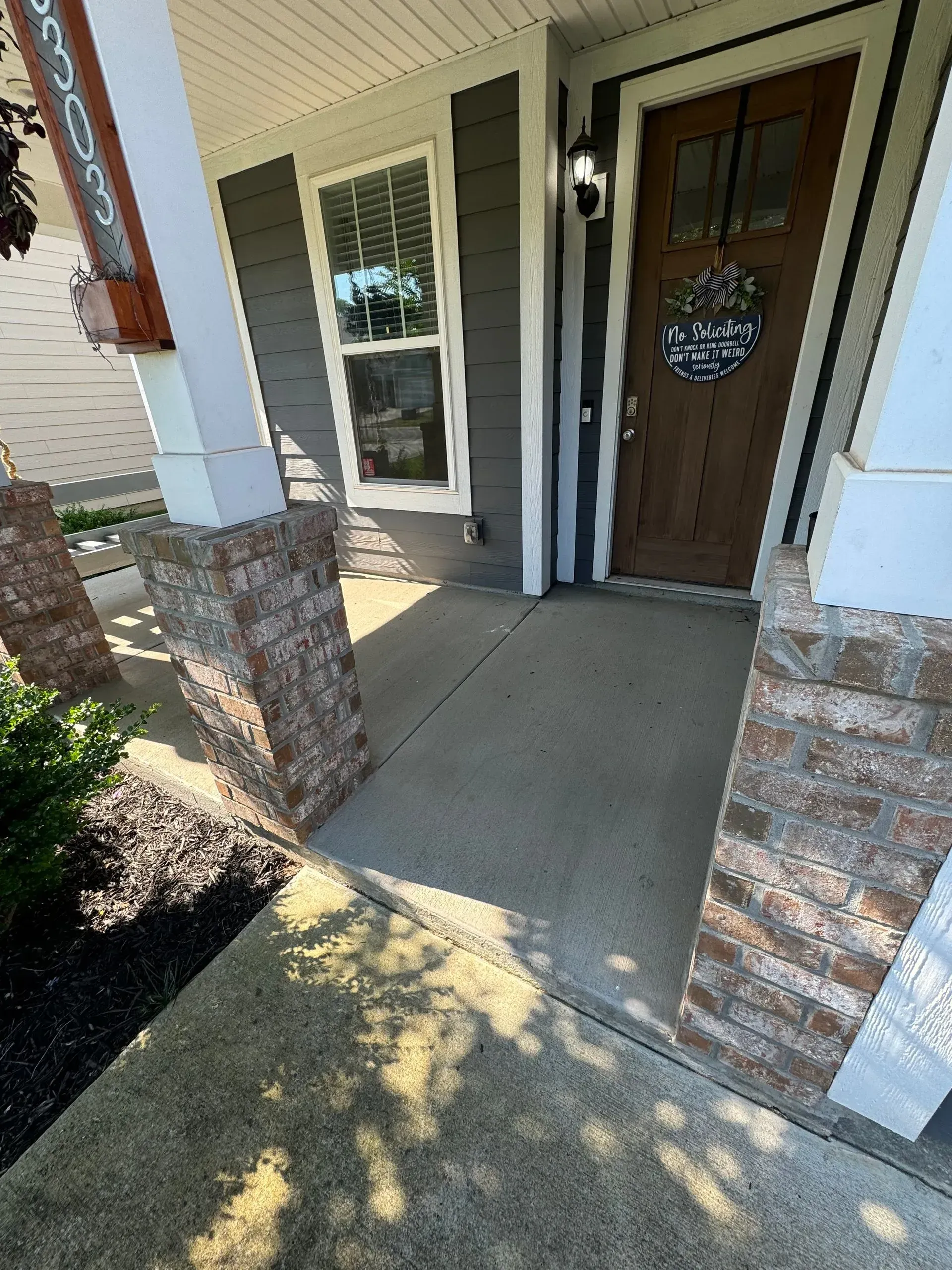 Front porch with brick columns, concrete path, wooden door with wreath.