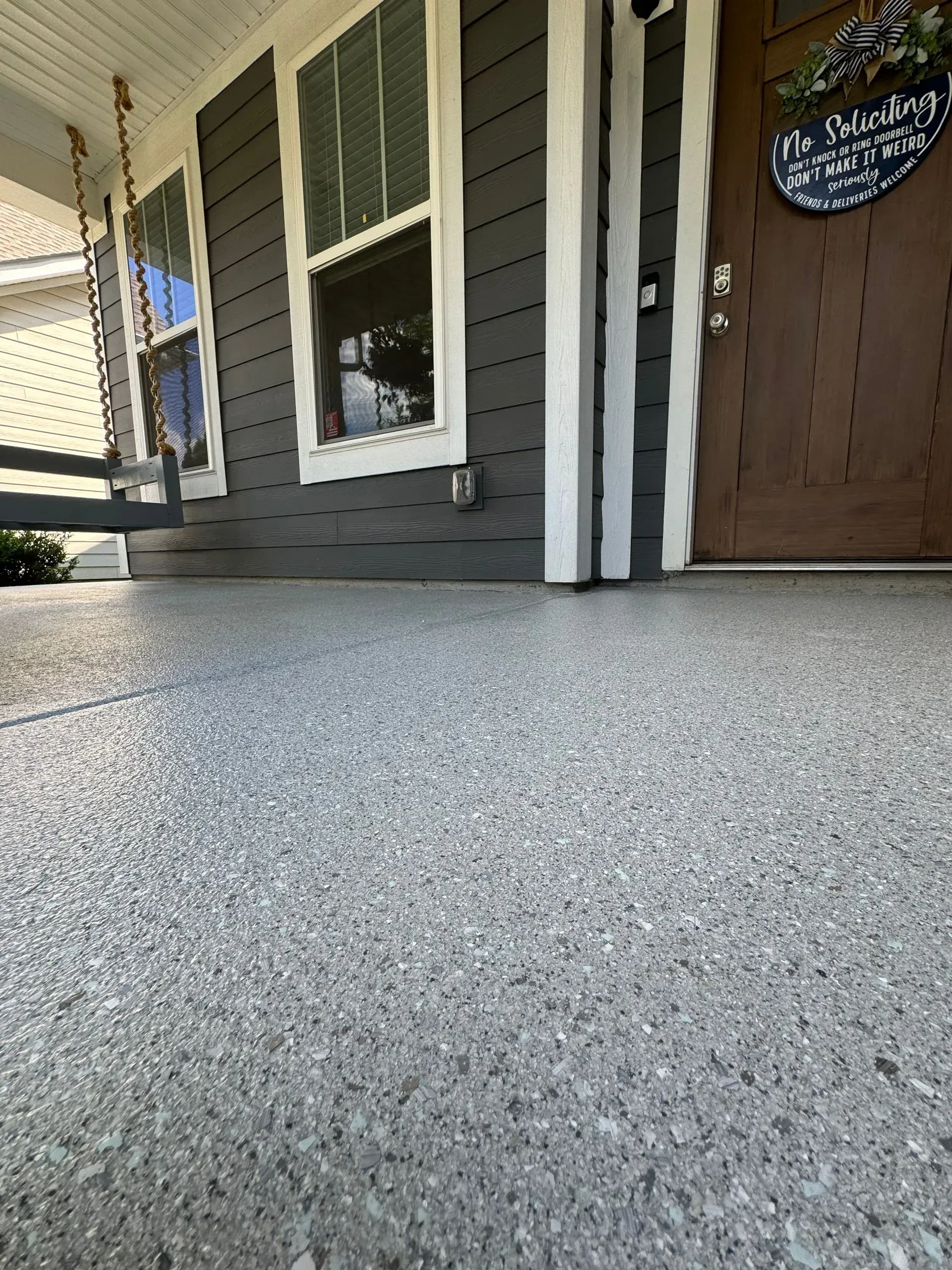 Gray speckled porch floor leading to a dark gray house with a brown door and a porch swing.