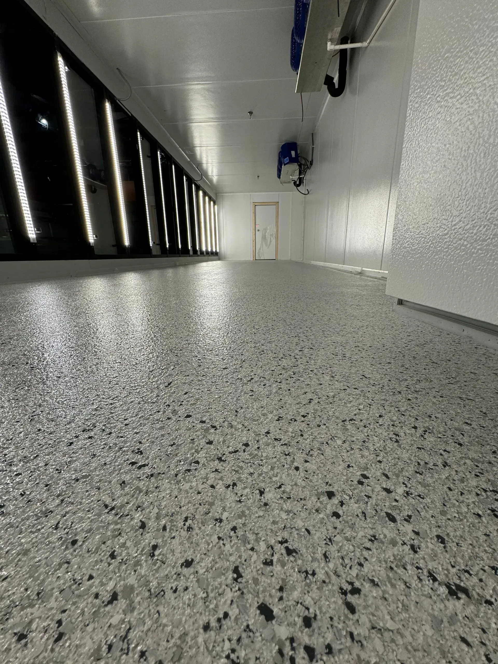 Long, narrow room with speckled gray floor, white walls, and bright overhead lighting.