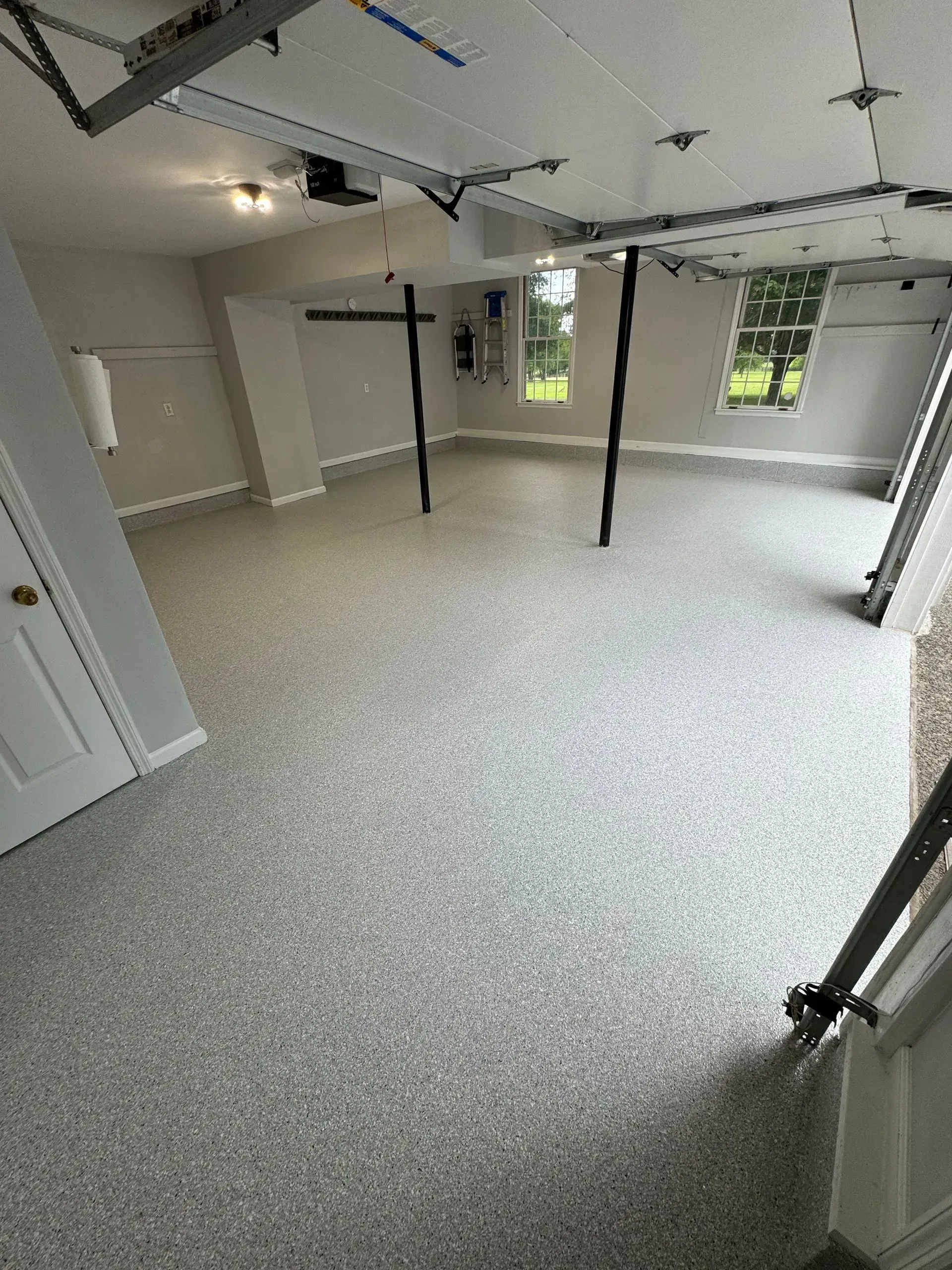 Spacious garage with gray speckled epoxy floor, light gray walls, and two windows.
