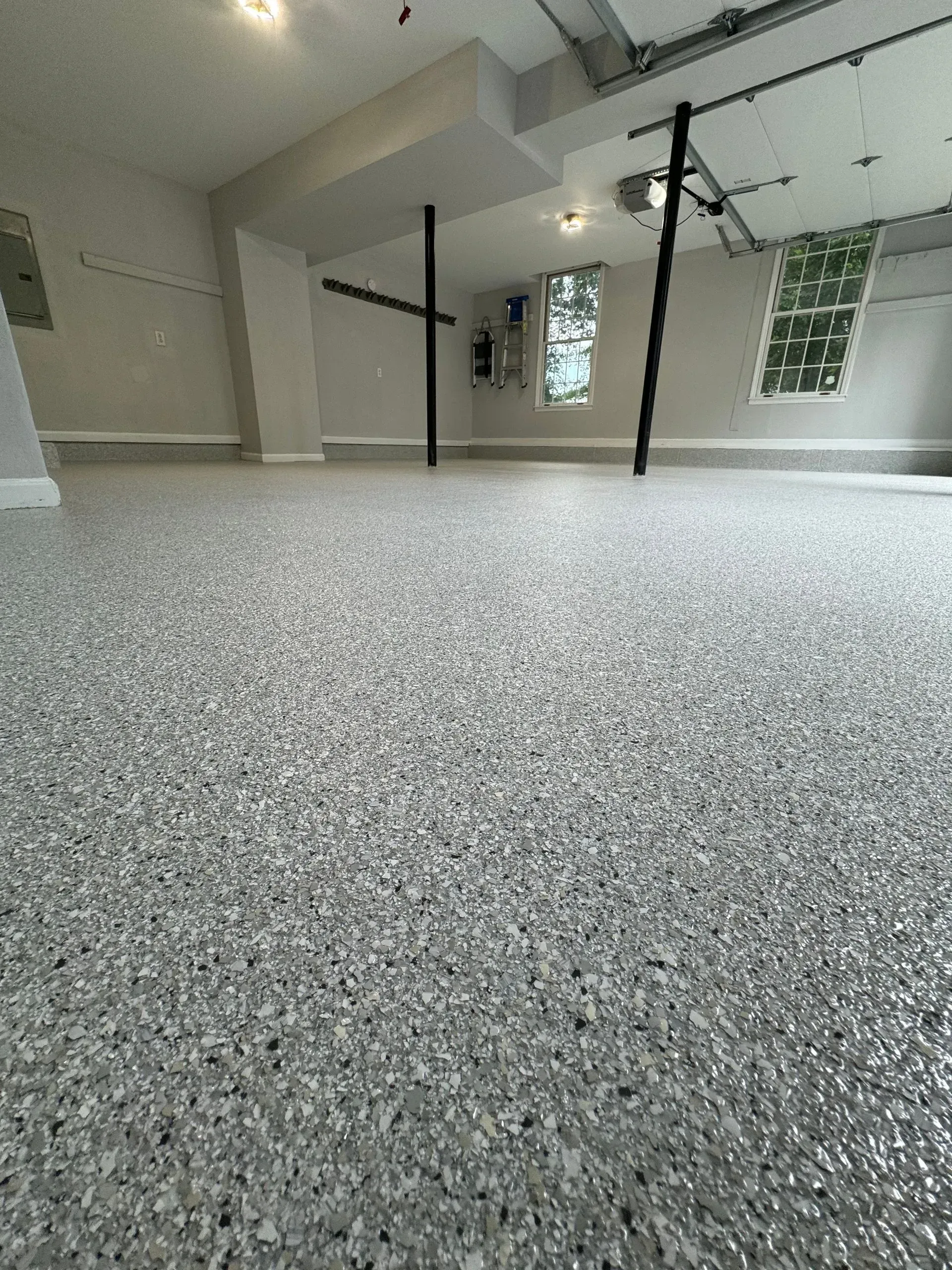 Garage interior with gray speckled epoxy floor, light gray walls, and black support beams.