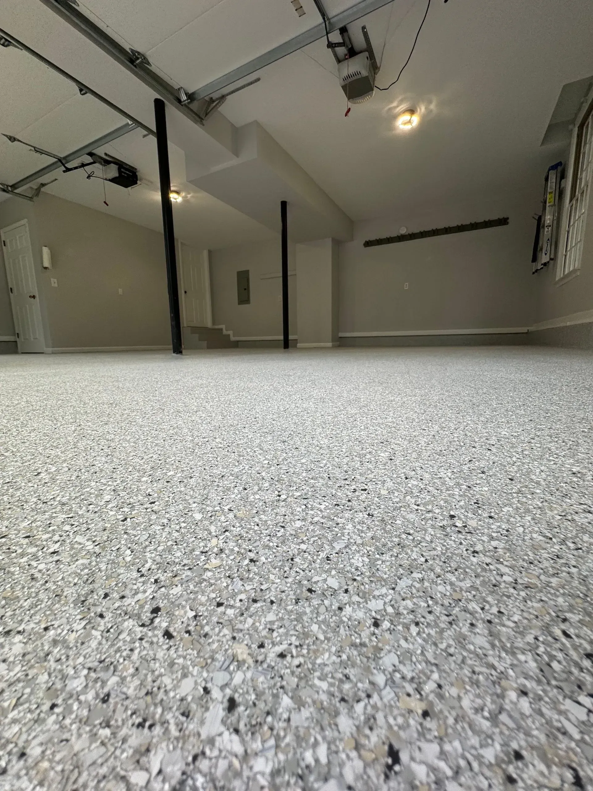 Empty garage with speckled epoxy floor and support beams.