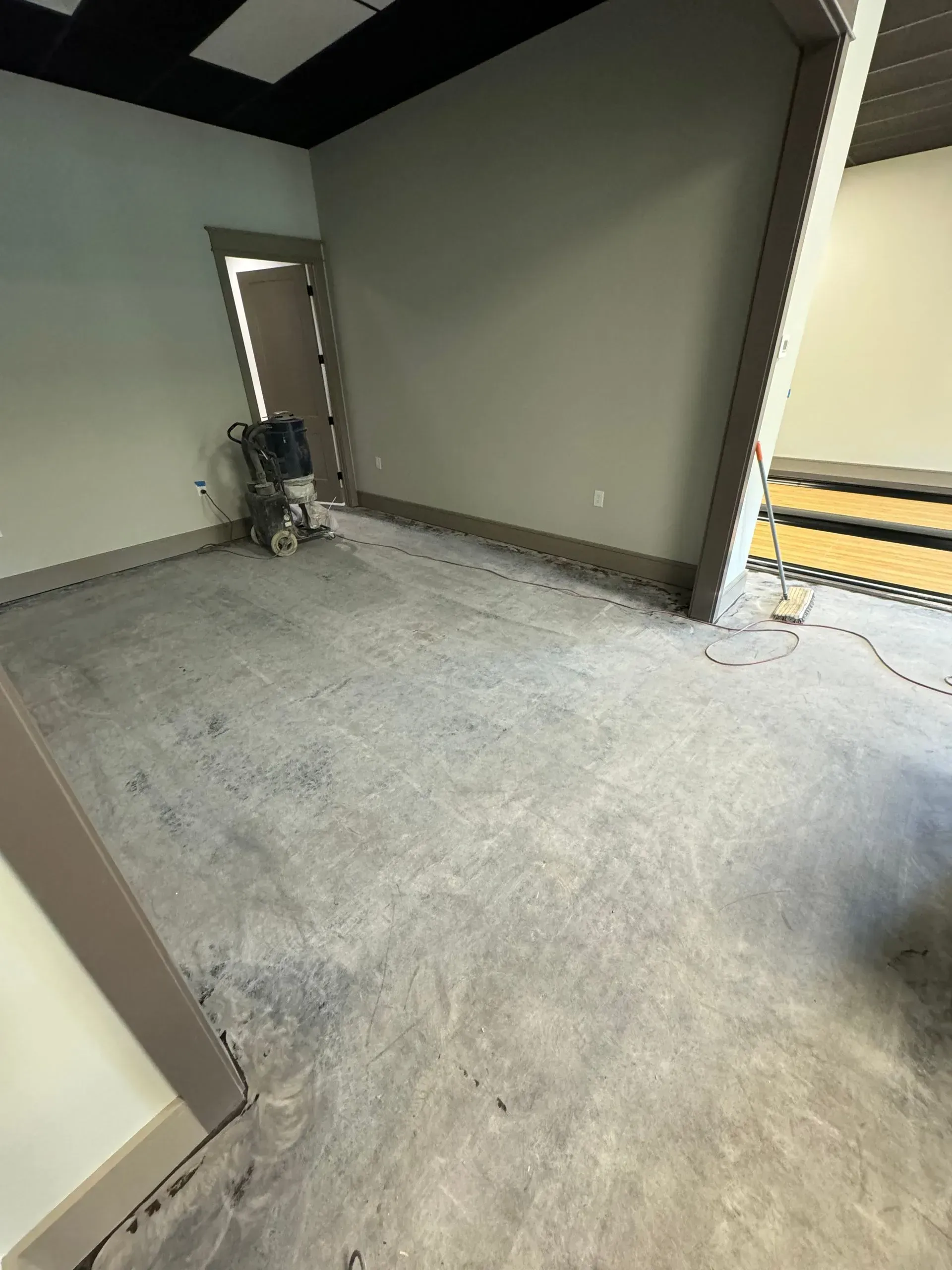 Room with concrete floor, walls and door frames painted light colors; a floor grinder is in the doorway.