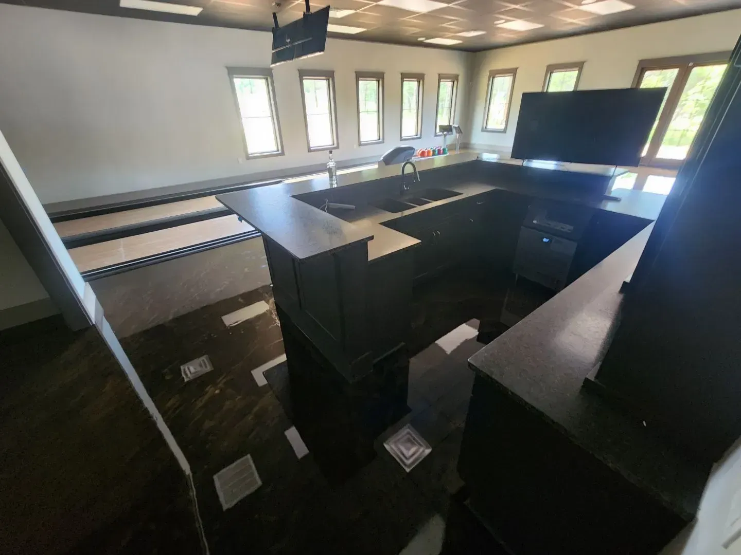 Dark-stained u-shaped bar with sink and large TV in a room with bowling lane floors.
