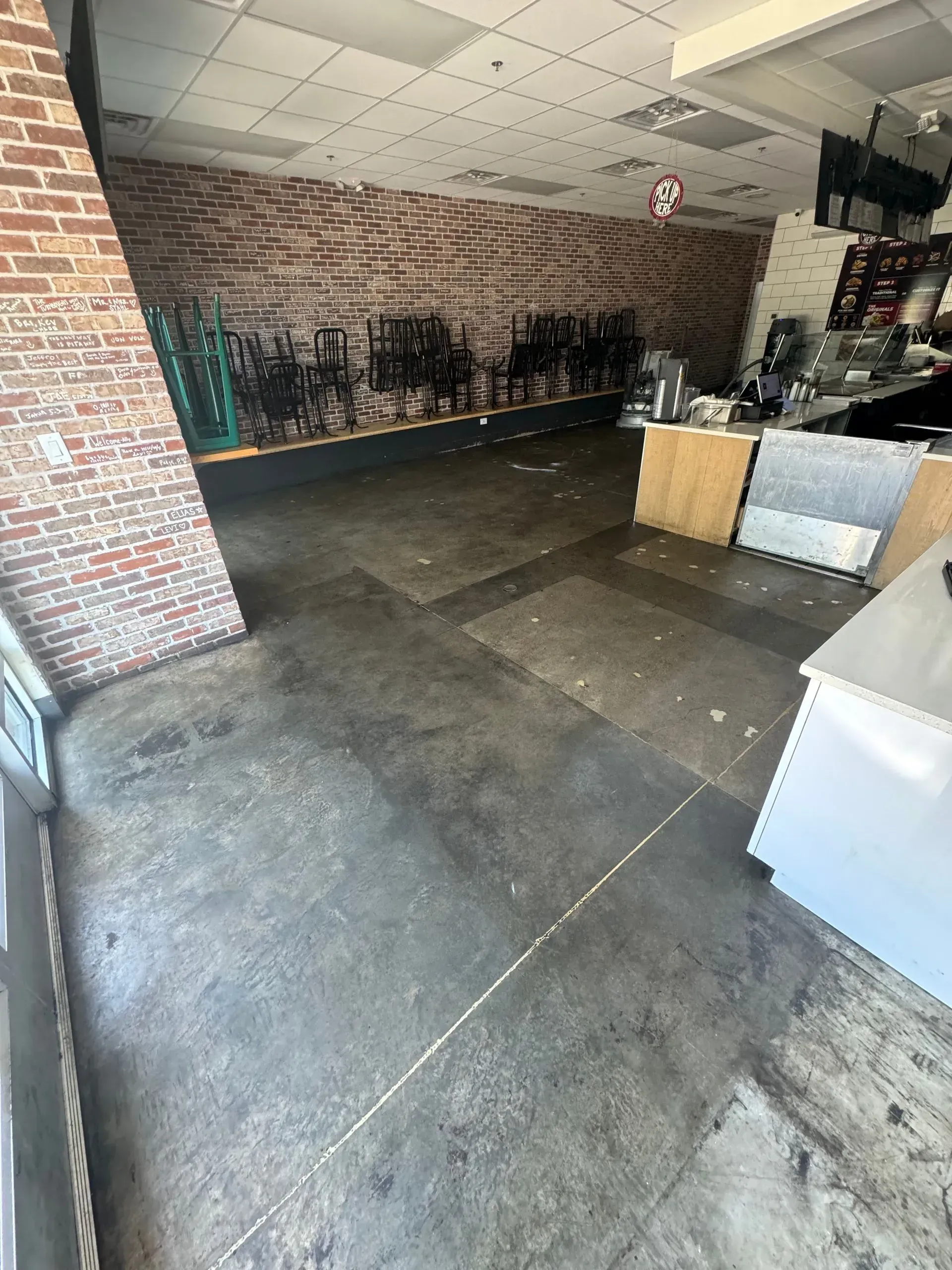 Empty interior of a cafe. Brick wall, bare concrete floor, counter, chairs, and empty space.
