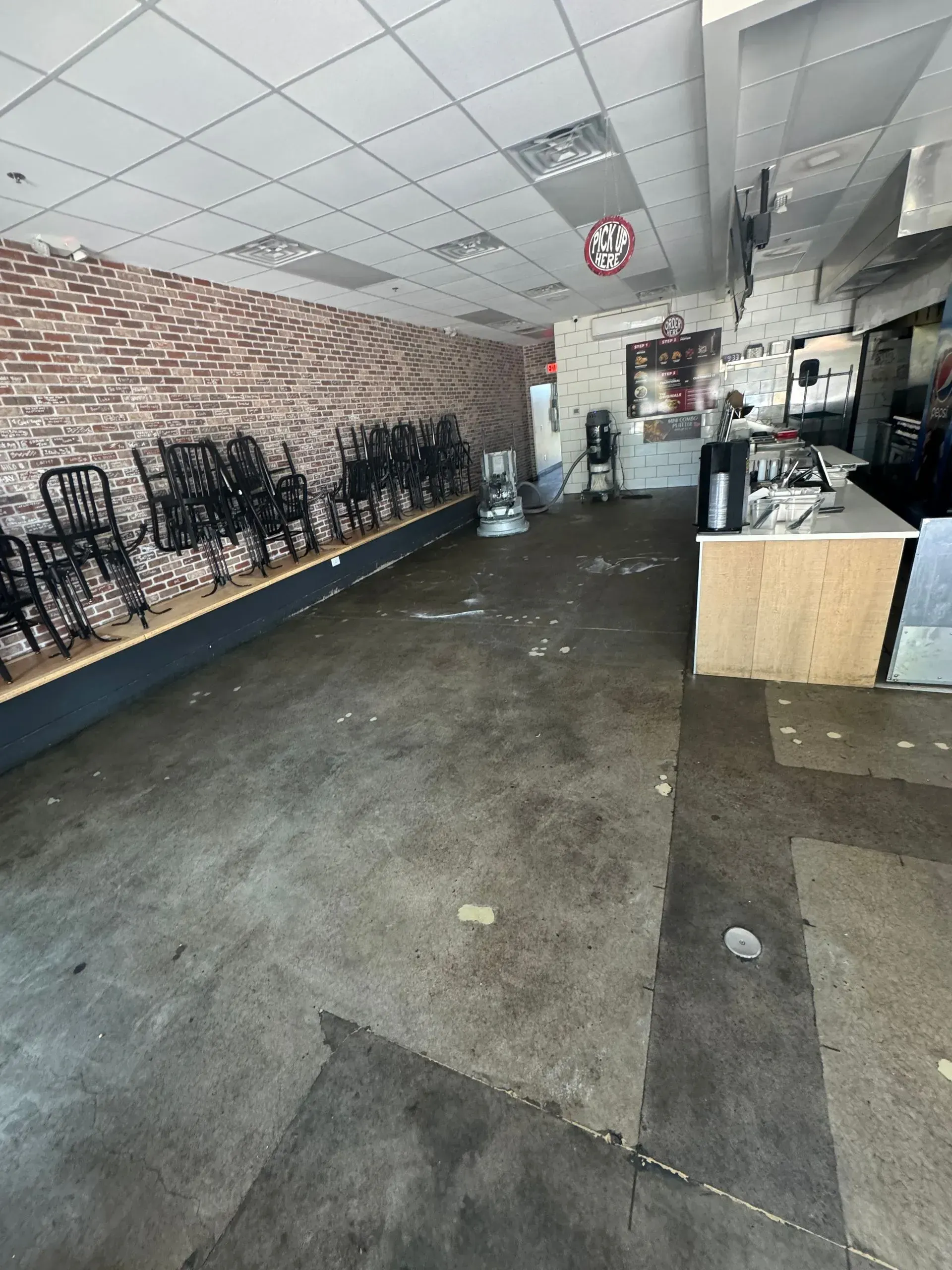 Empty restaurant interior with dark floor, brick wall, and stacked chairs.