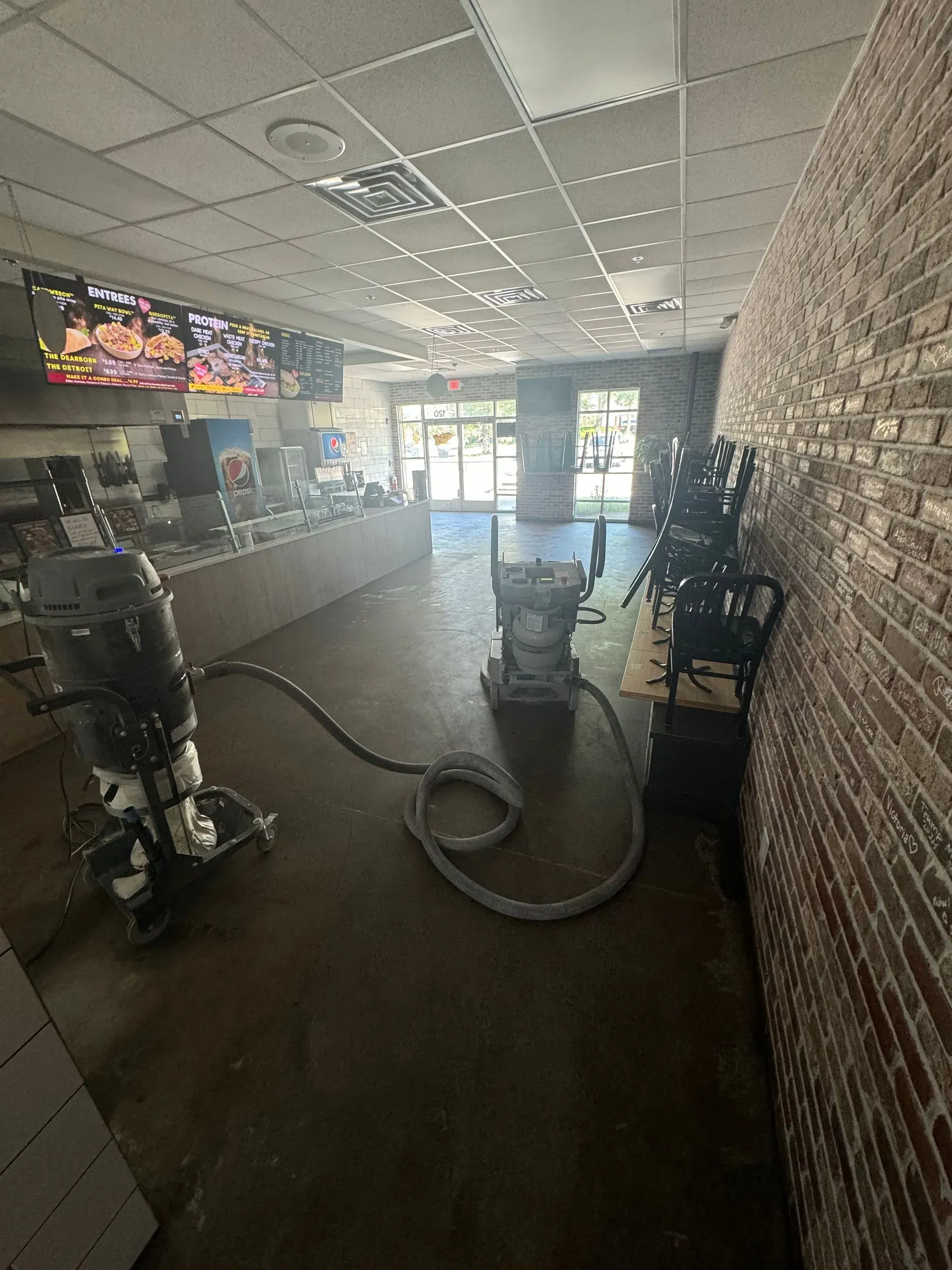 Restaurant interior with concrete floor being resurfaced; floor grinder, brick wall.