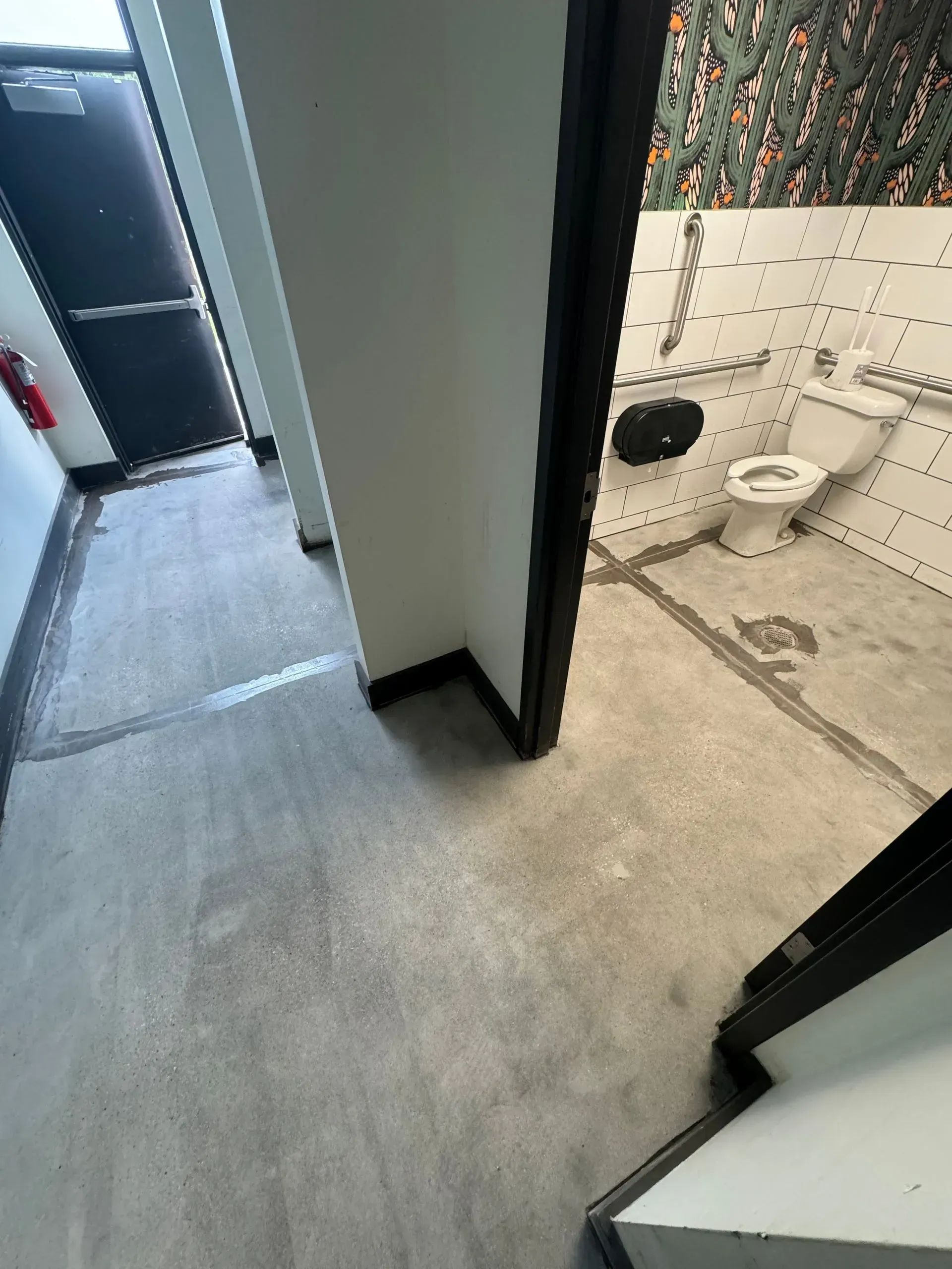 Hallway leading to a bathroom with a toilet. Concrete floors, white walls, black door frames.