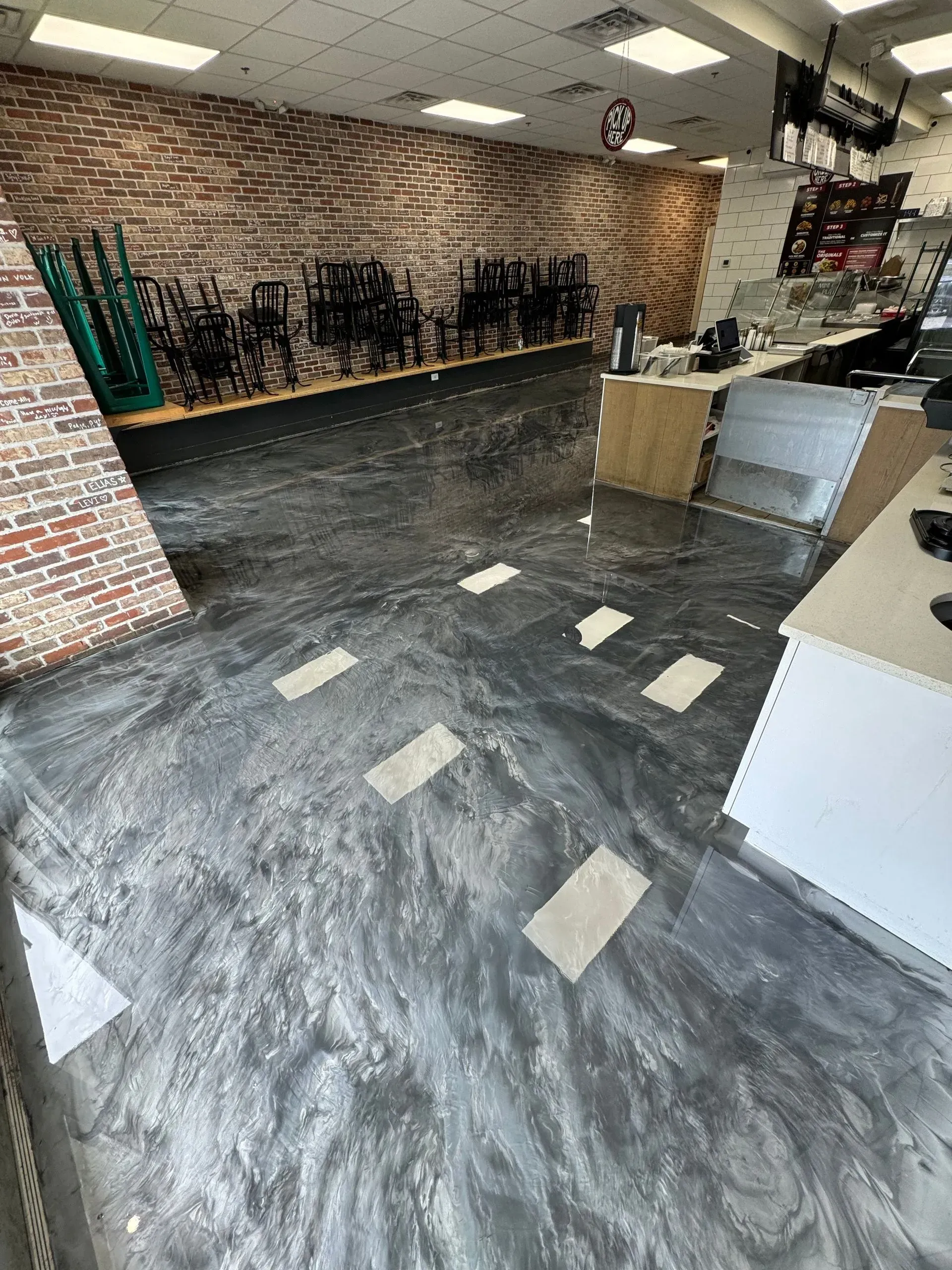 Shiny gray epoxy floor in a shop, brick wall, white counters, and display racks with equipment.