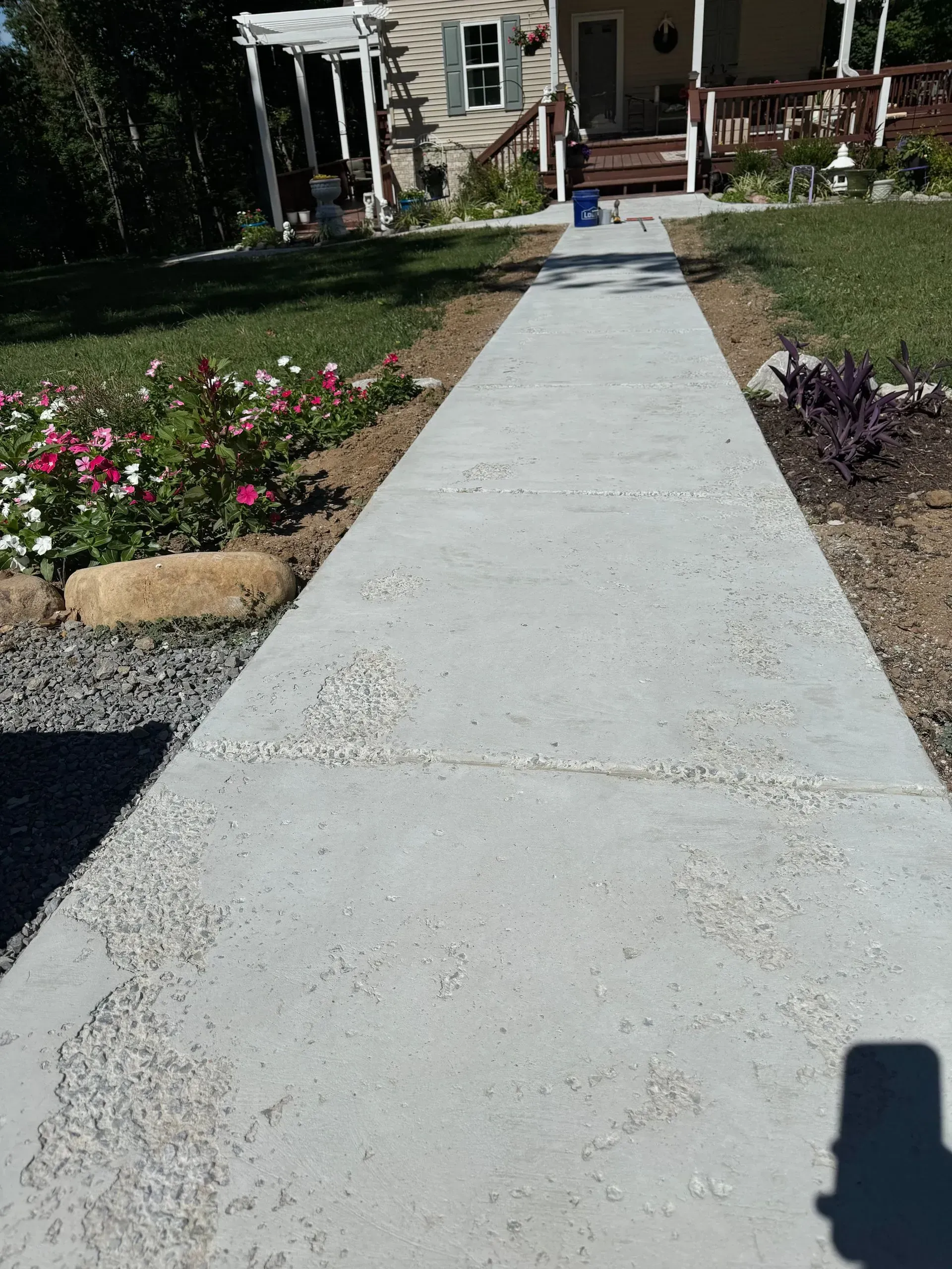 A concrete walkway leads to a house with a porch, flanked by landscaping and gravel.