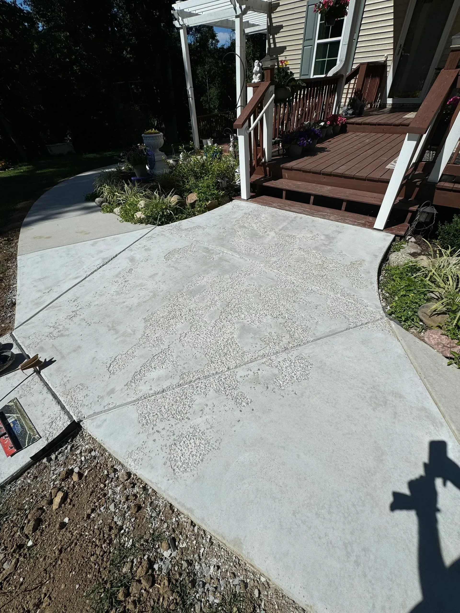 Gray concrete pathway leading to a house with a small porch and steps; sunny outdoor setting.