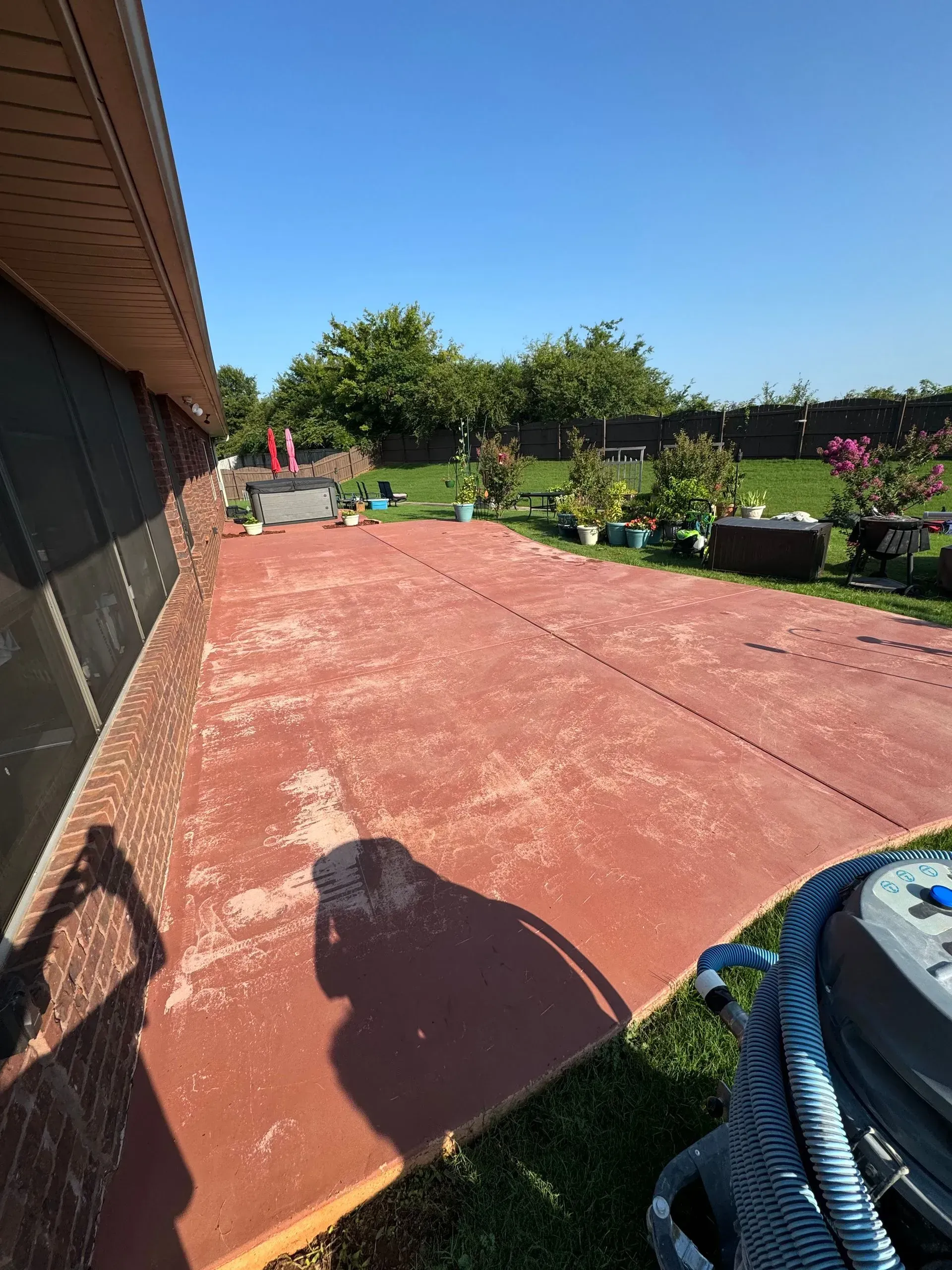 Red concrete patio with peeling paint, beside a brick wall under a bright blue sky.
