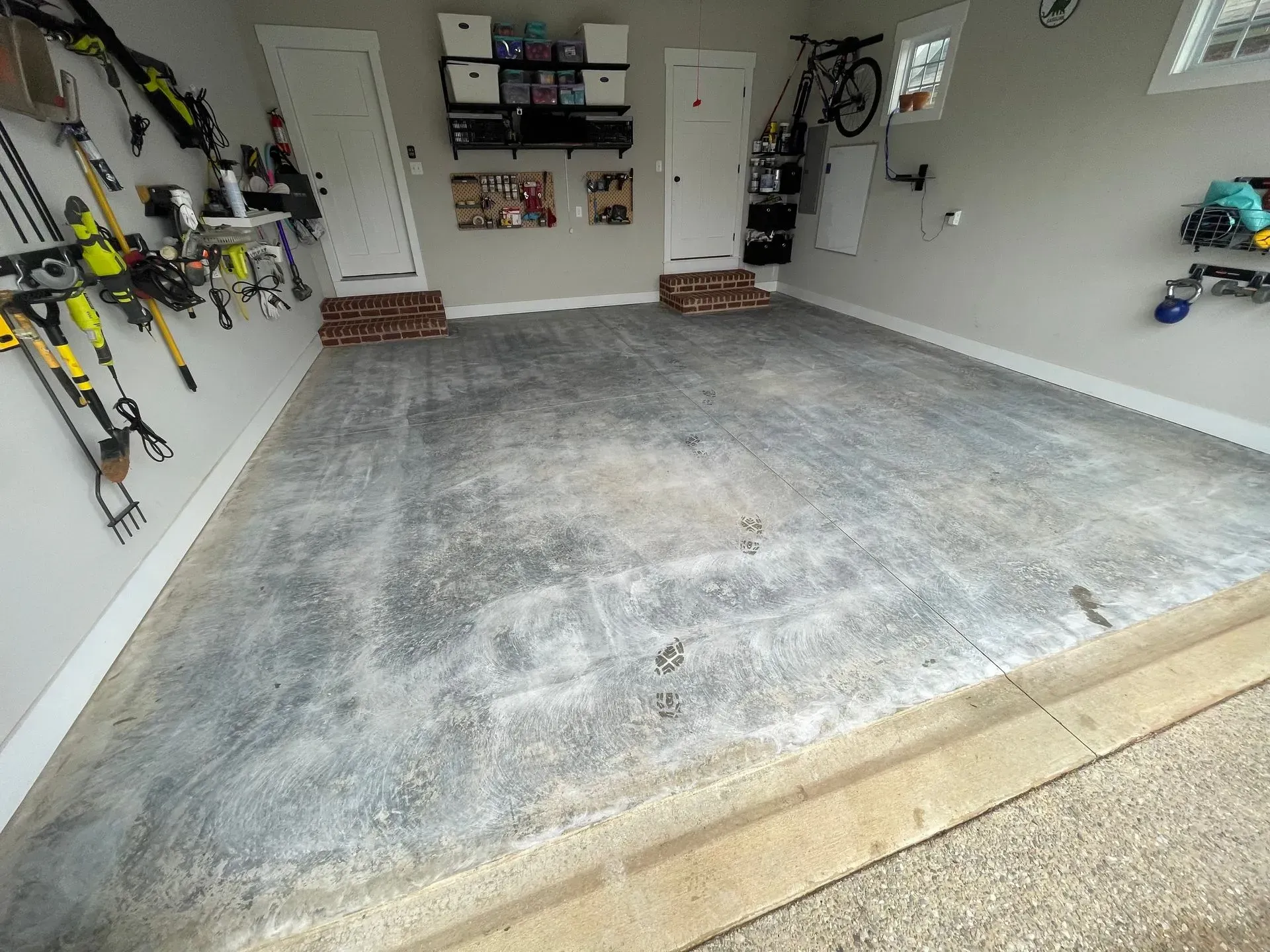 Garage interior: Concrete floor, tools on walls, storage shelves, bicycles. Gray, white, beige.