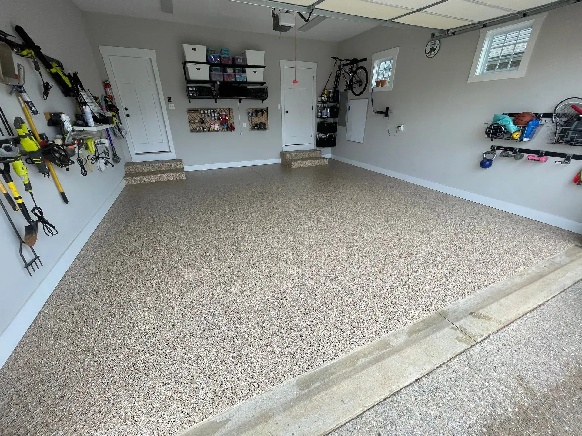 Garage with a speckled floor, white walls, and doors. Ski gear and tools mounted on walls.