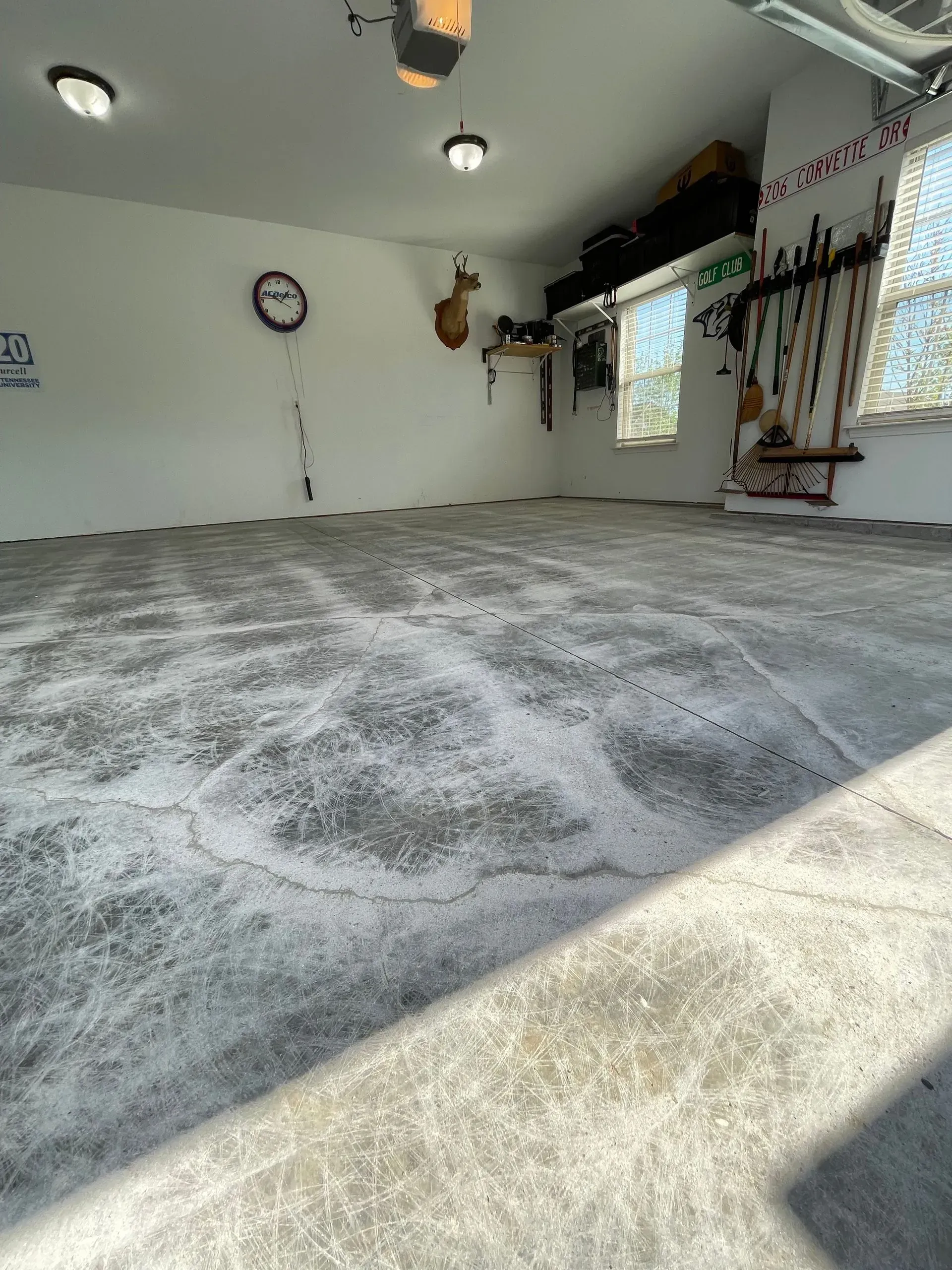 An empty garage with a textured, gray floor, white walls, and a few decorations; lit by ceiling lights.