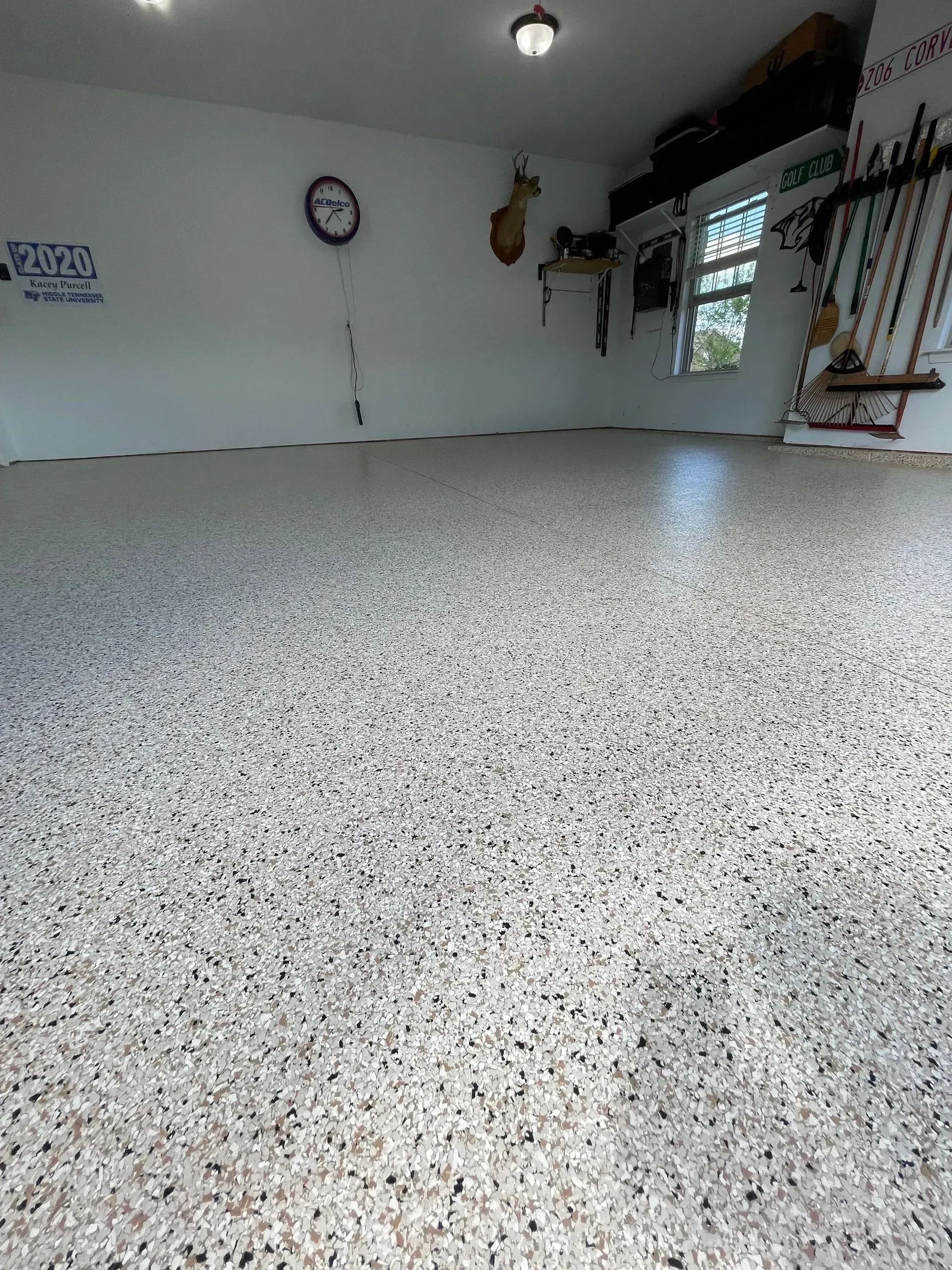 Garage interior with speckled flooring; white walls, a clock, deer mount, and tools are visible.