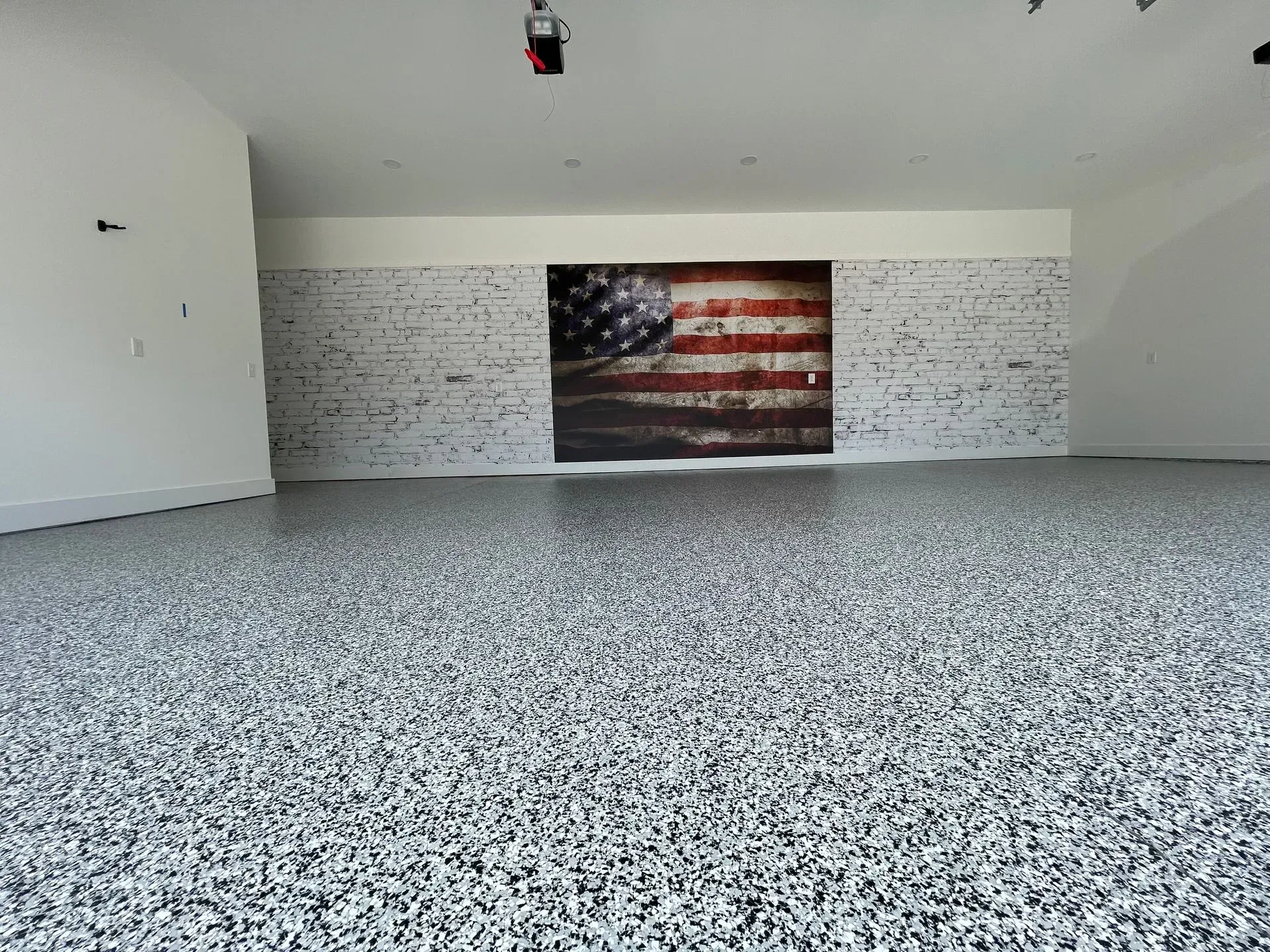 Garage with gray speckled epoxy floor, brick wall, and American flag art.