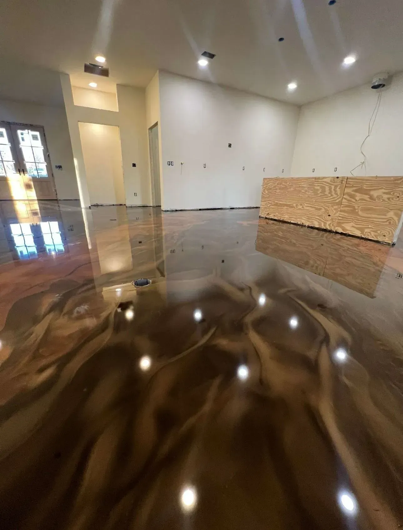 Metallic epoxy floor in a room with white walls, reflecting lights and a wood panel.