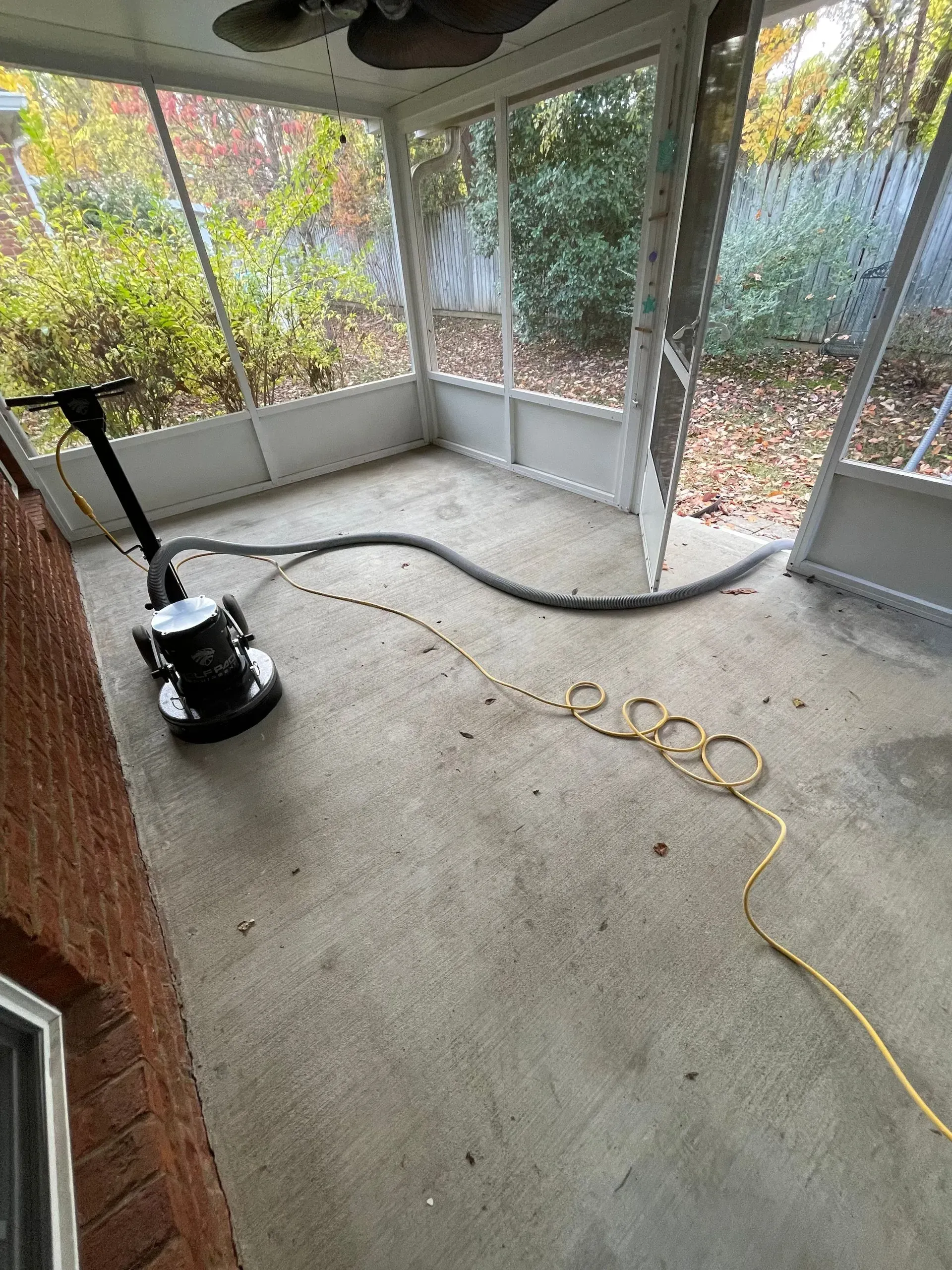 A floor buffer on a concrete porch, with a hose and power cord, ready for cleaning.