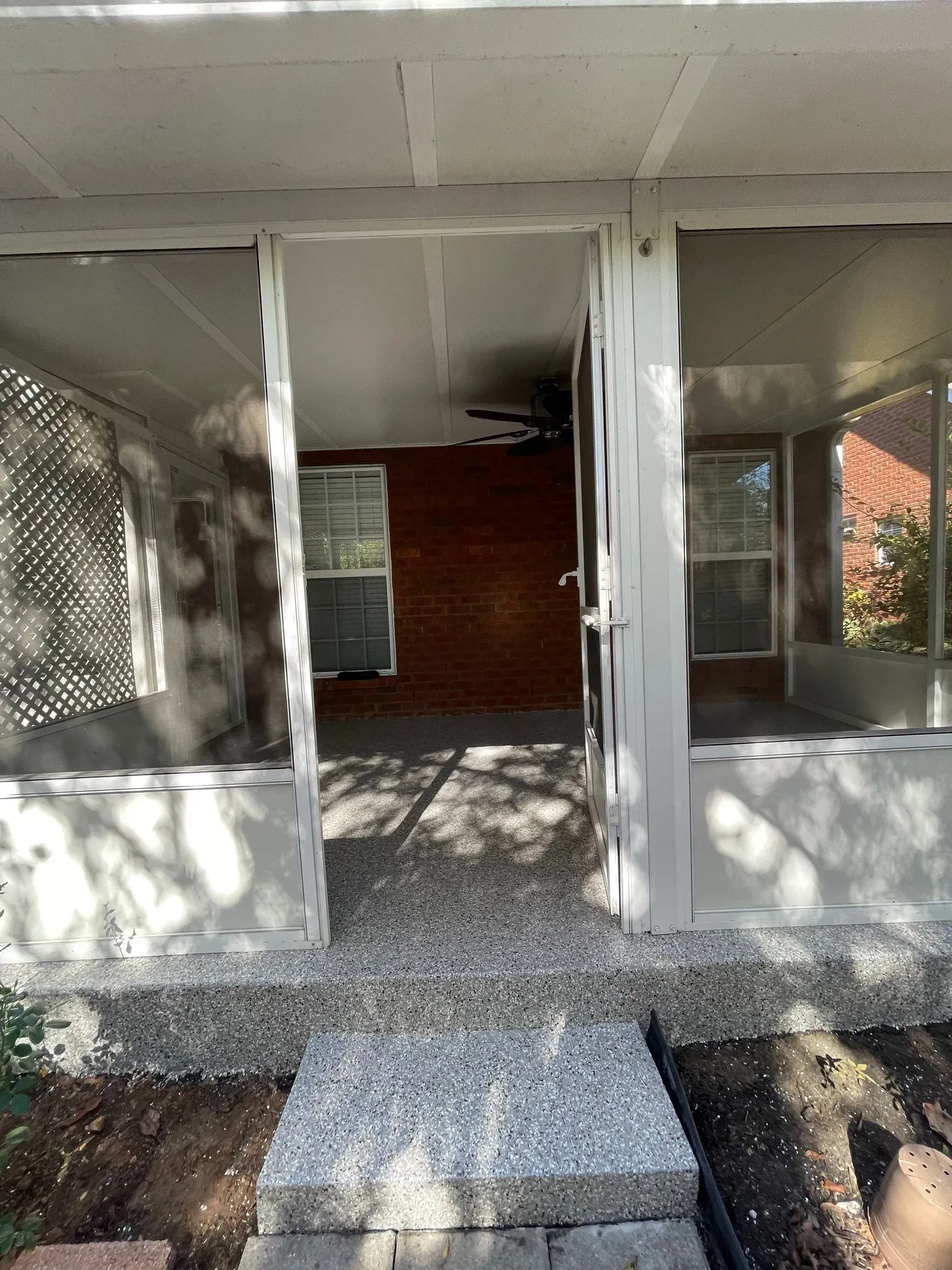 A doorway leads into a screened-in porch with a concrete threshold and gravel path.