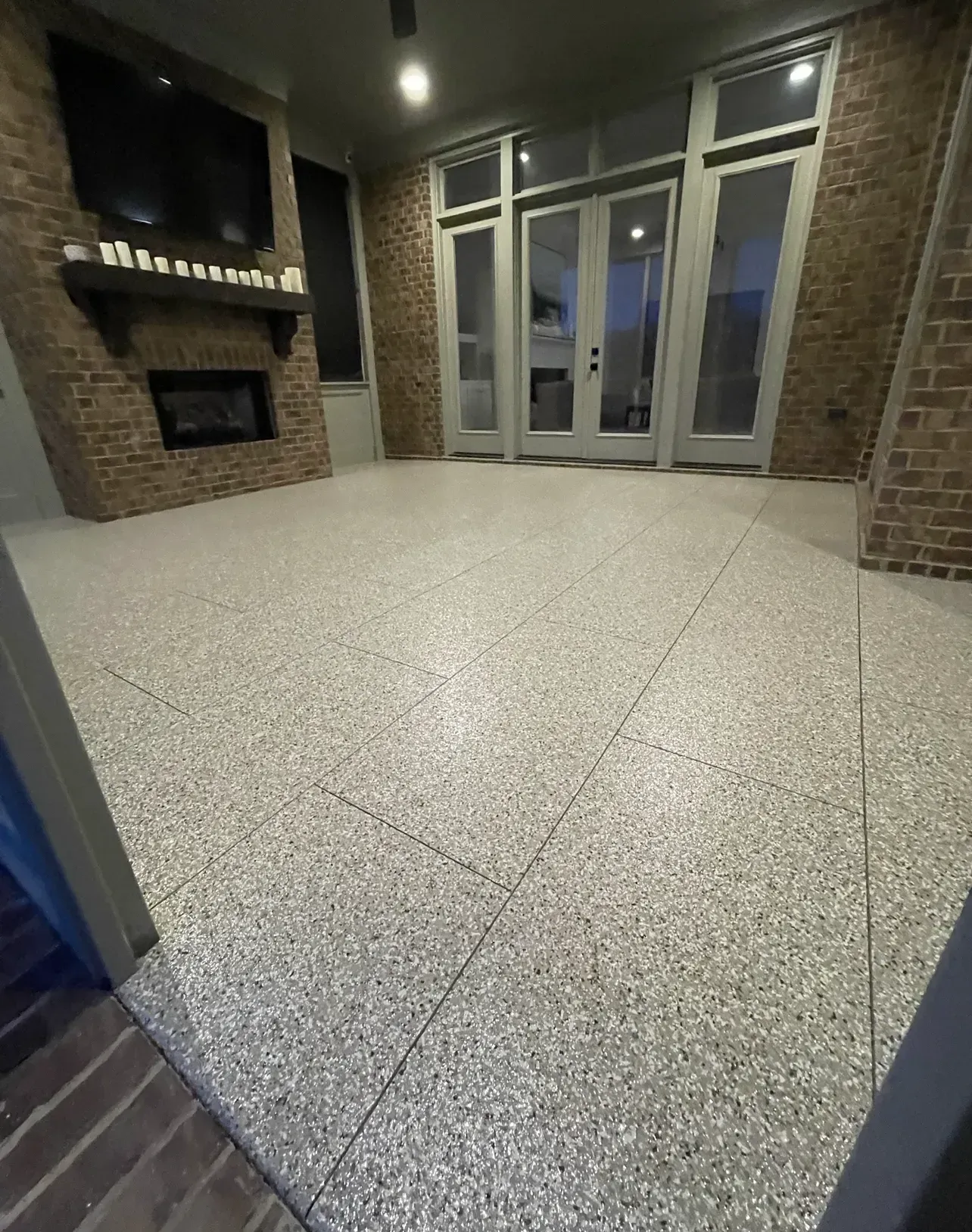 Spacious outdoor patio with a fireplace, glass doors, and speckled gray flooring.