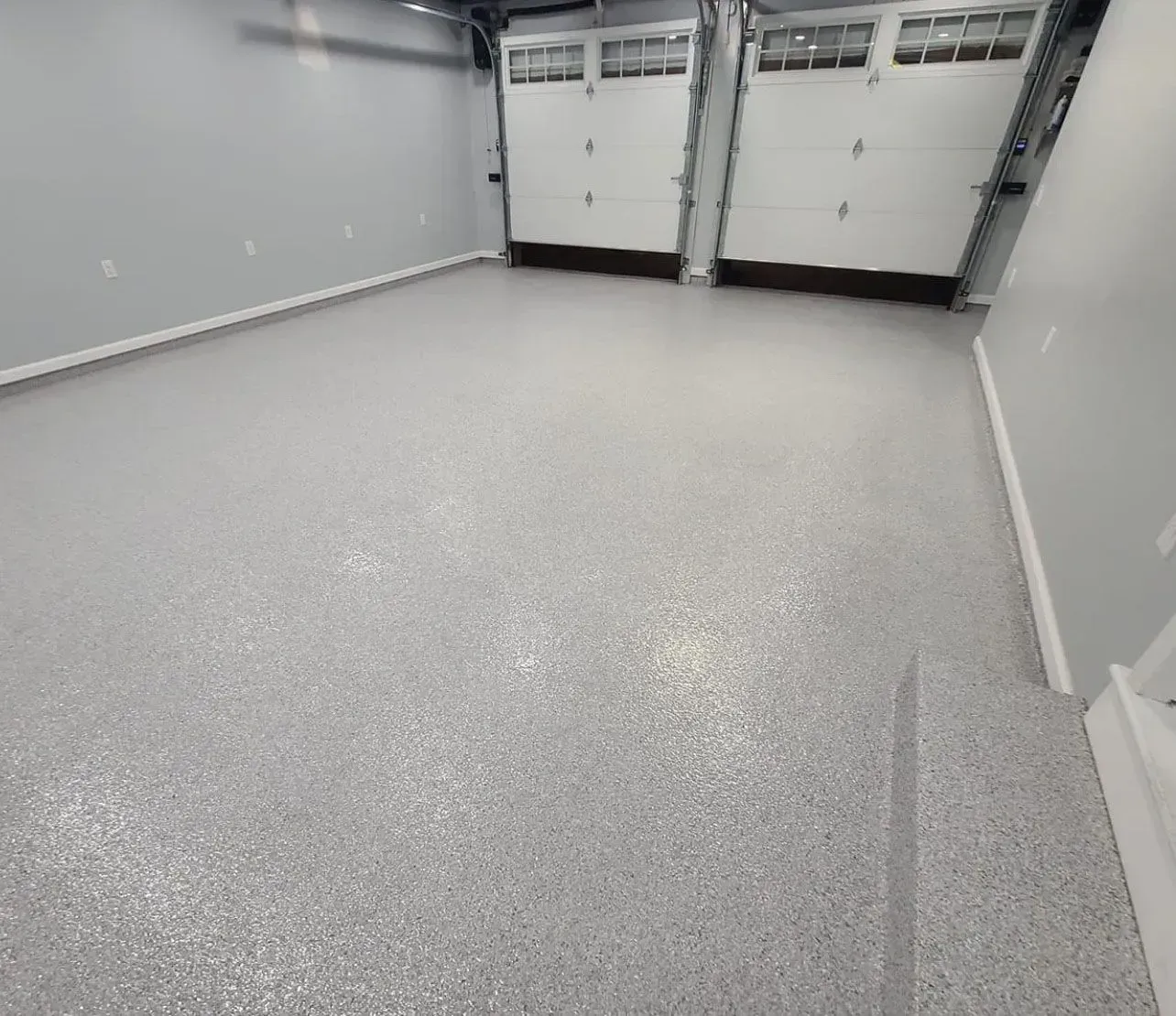 Garage with a speckled, light gray epoxy floor. White garage doors are visible.