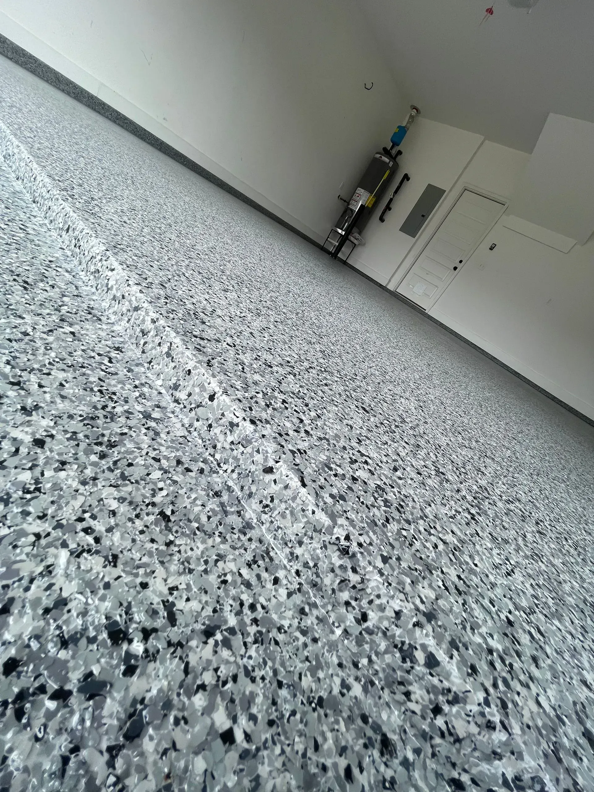 Gray and black speckled floor in a bright room, angled view with a bicycle and white walls.